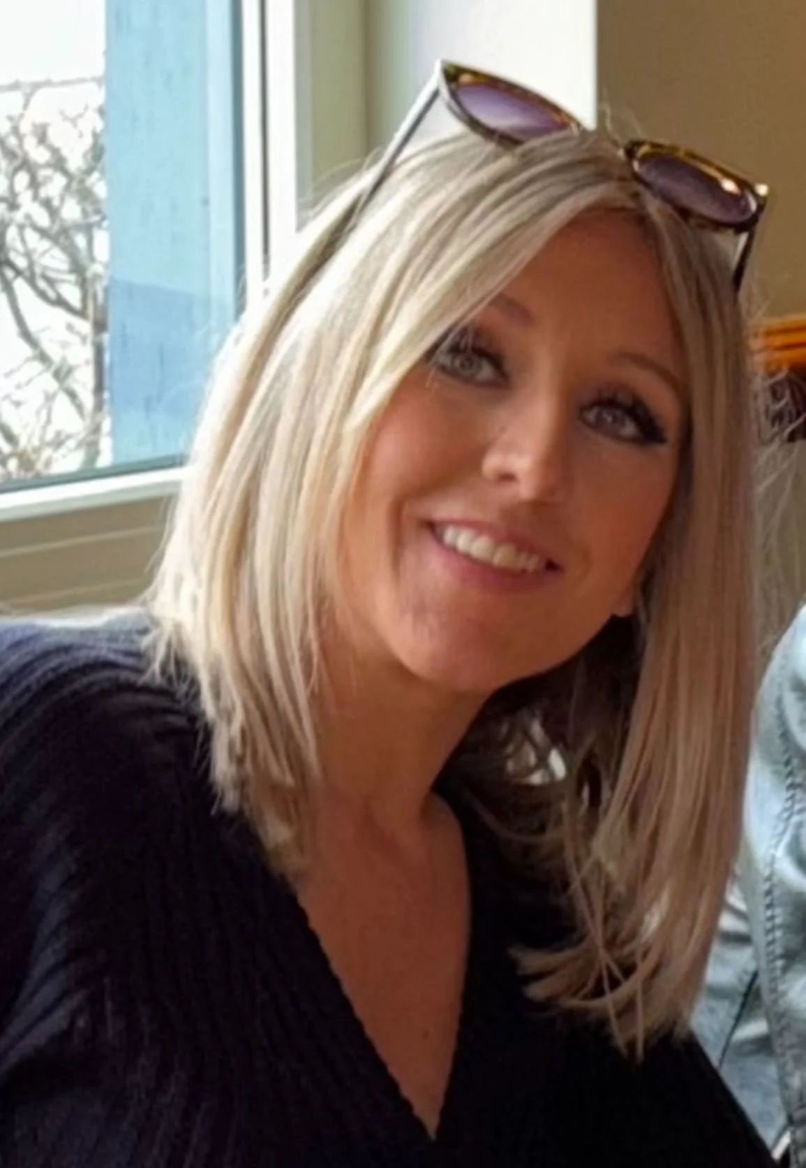 Zoe Warnes has a long straight blonde bob and is wearing a black v neck jumper