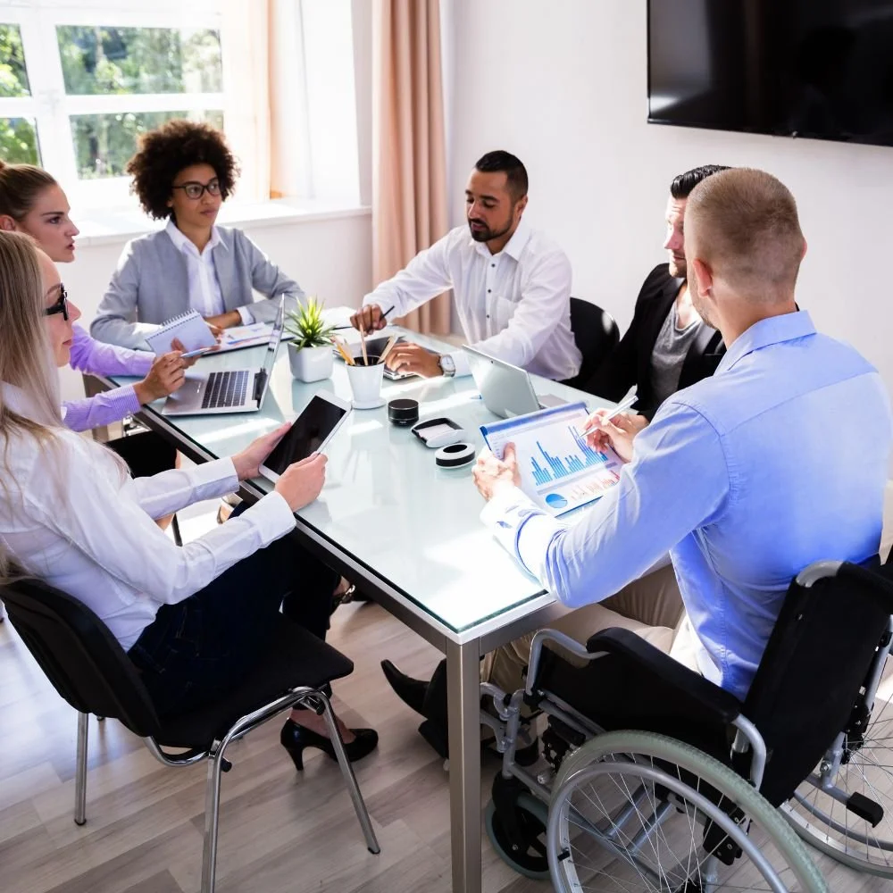 A team sat around a table discussing marketing plans with a male on the marketing executive apprenticeship who is in a wheelchair