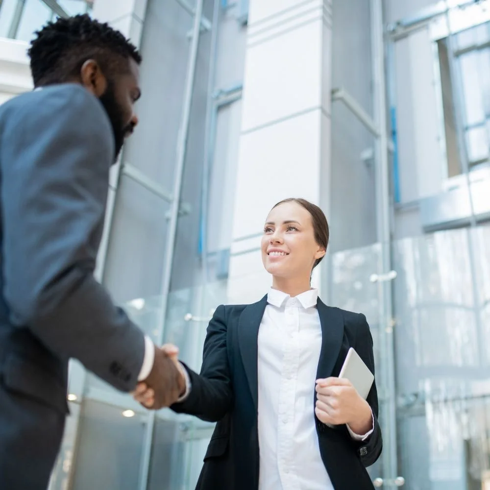 Black man in suit shaking hands with young whit woman in a suit for the new term