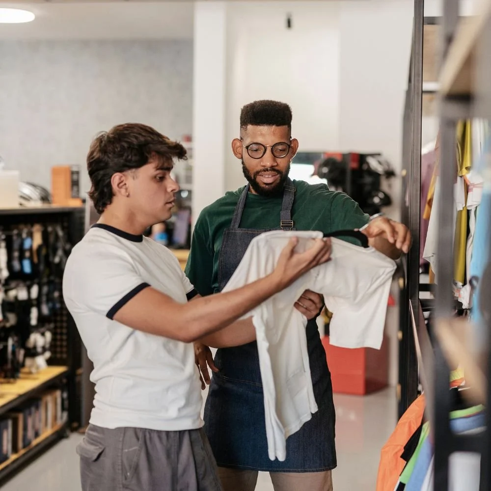 A male retail assistant in a sports shop helping a male customer with a t-shirt during a Retailer Apprenticeship