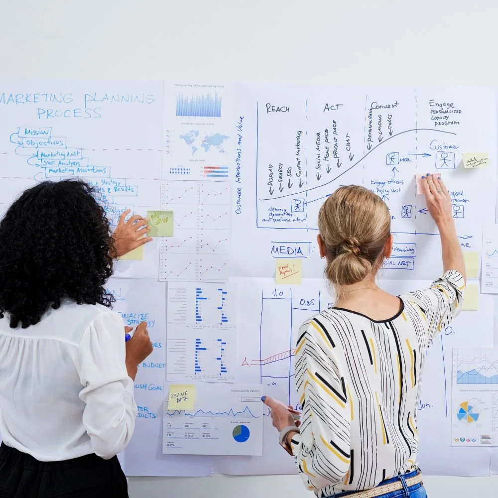 An Apprentice on the Mmarketing Executive Apprenticeship working with a colleaugue on a whiteboard, planning marketing