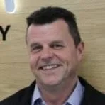 Gary Howard has short dark hair, is smiling direct to the camera wearing a blue shirt, tie and dark jacket