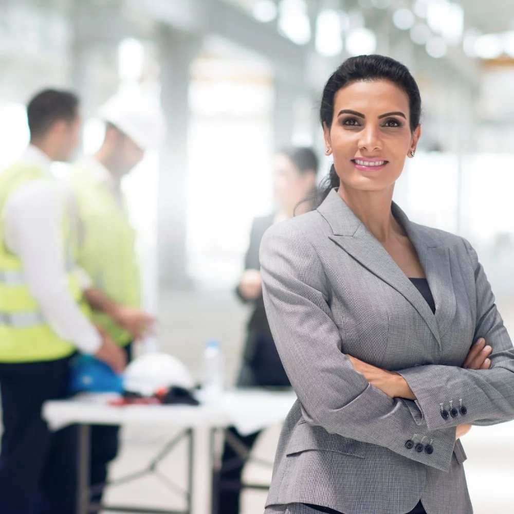 A business woman in the fore with people in high visibility vests in the background on the associate project manager apprenticeship