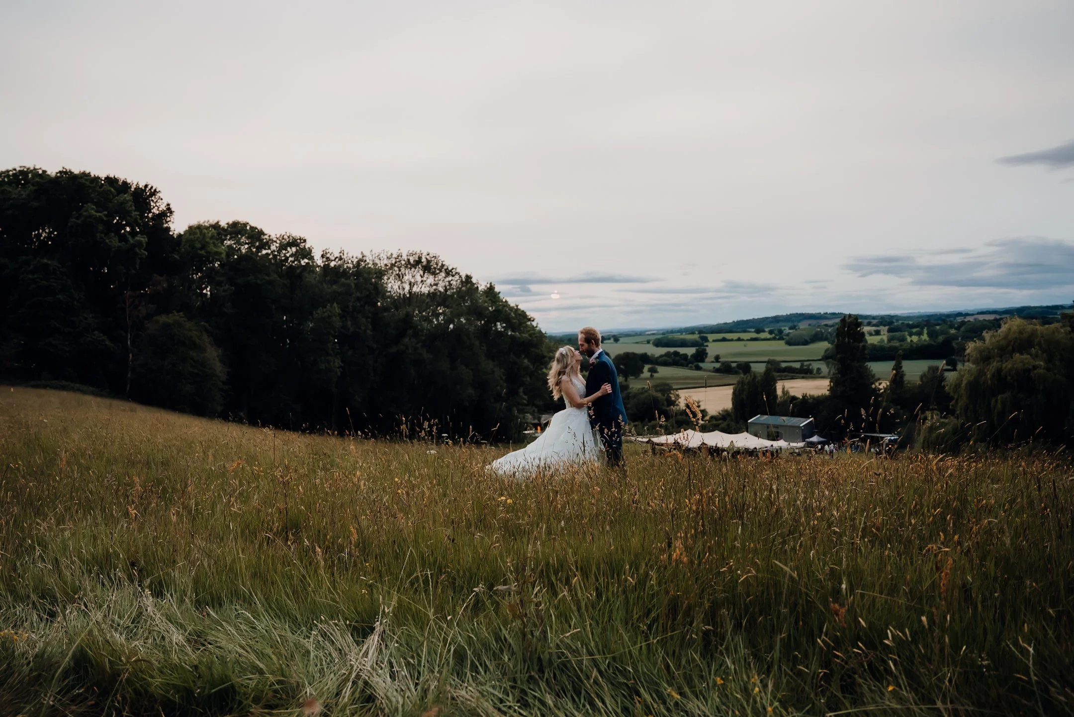 bride and groom embrase a landscape photo of them upon a hill with the stunning hills of herefordshire