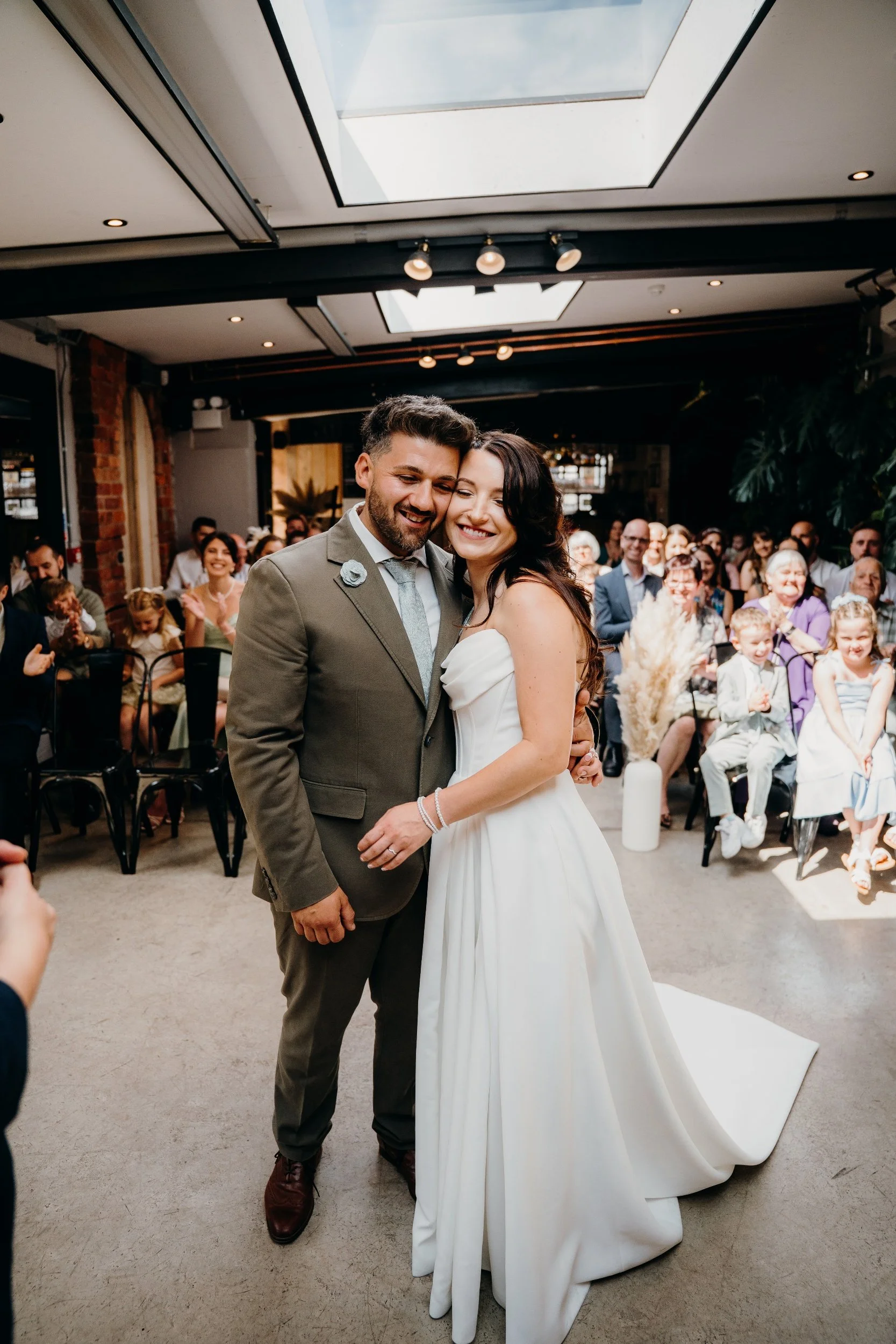 Bride and groom hugging during their wedding ceremony, with guests seated and smiling in the background.