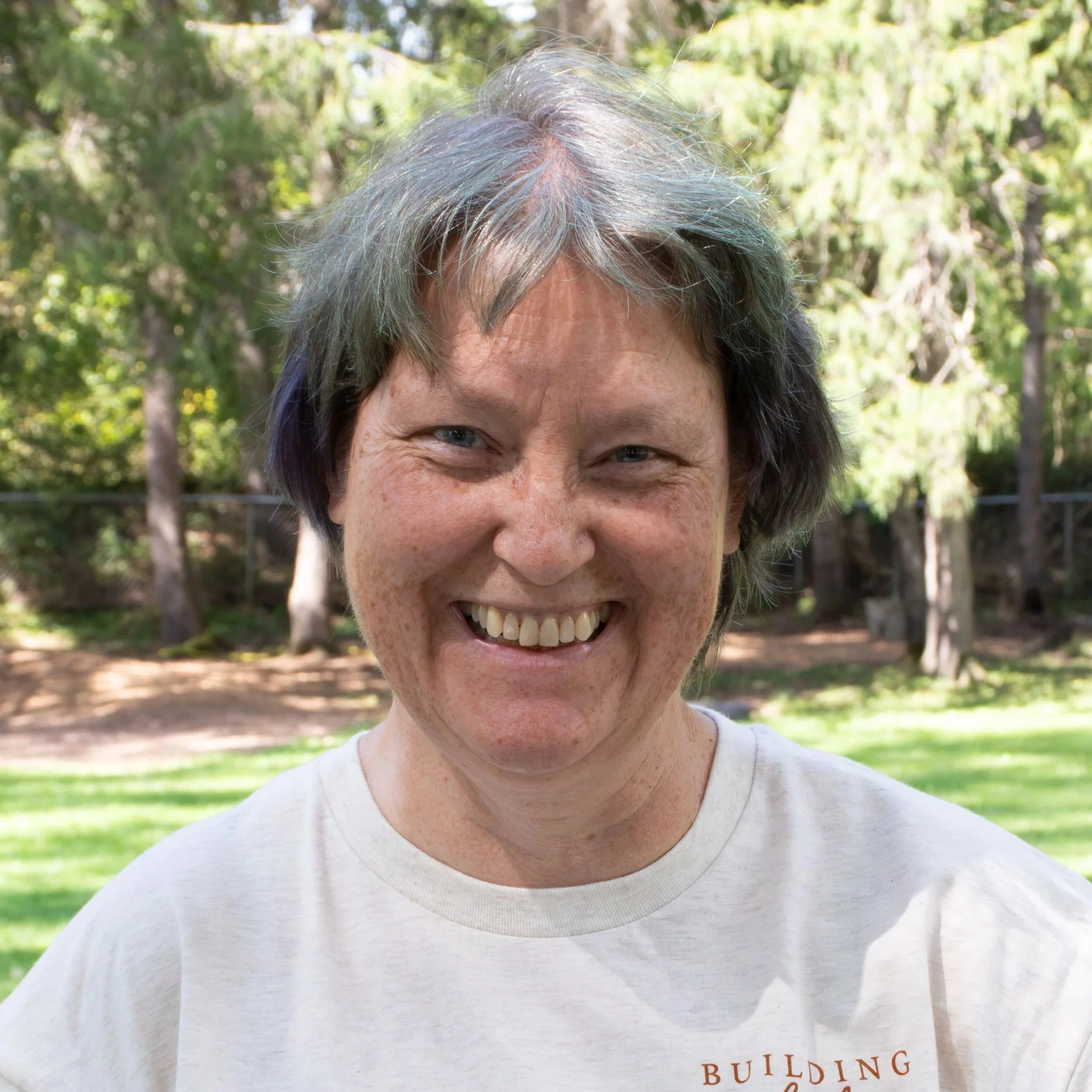 A woman with shoulder-length brown hair smiling, wearing a floral patterned top and a silver necklace.