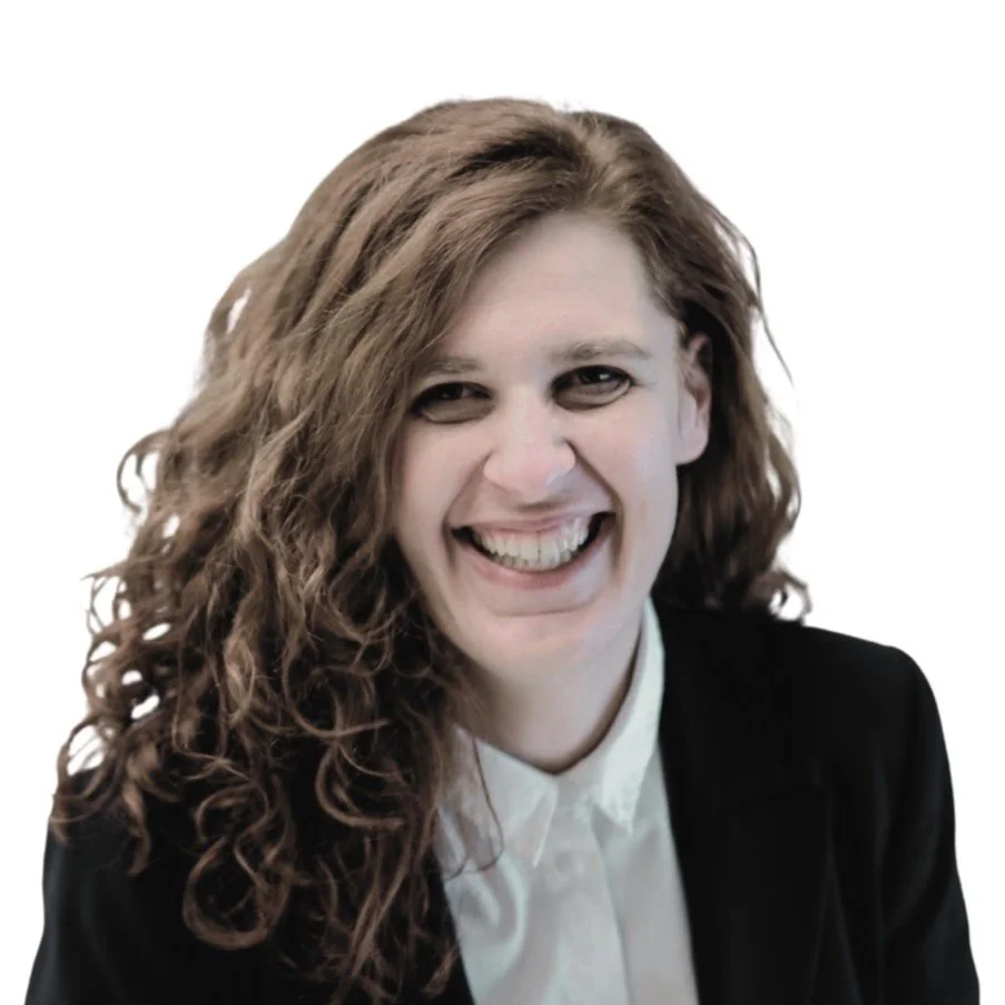 A woman with long, curly brown hair smiling and wearing a black blazer and white shirt against a plain white background.