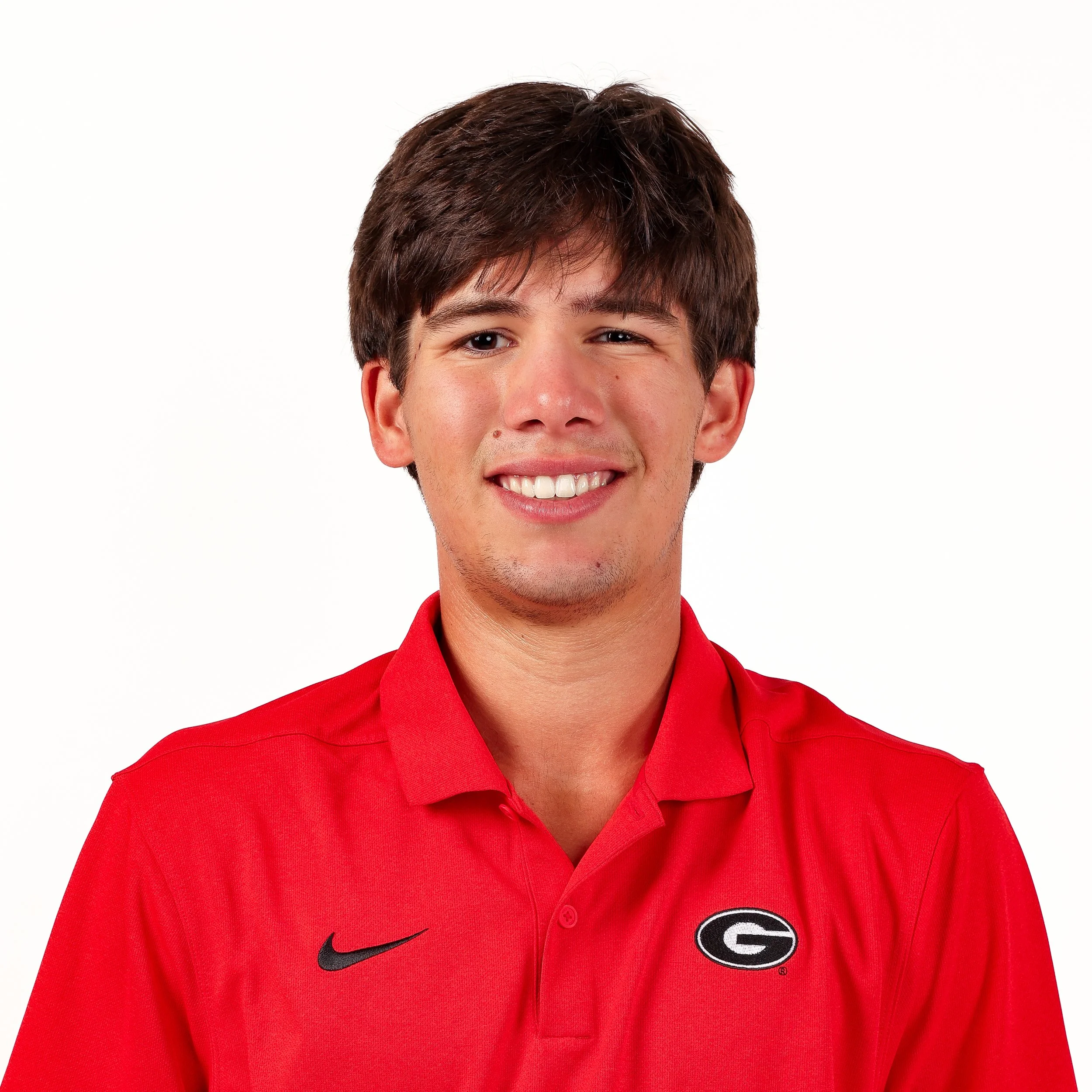 Close-up of a young man wearing a red University of Georgia Bulldogs polo shirt, smiling, against a white background.