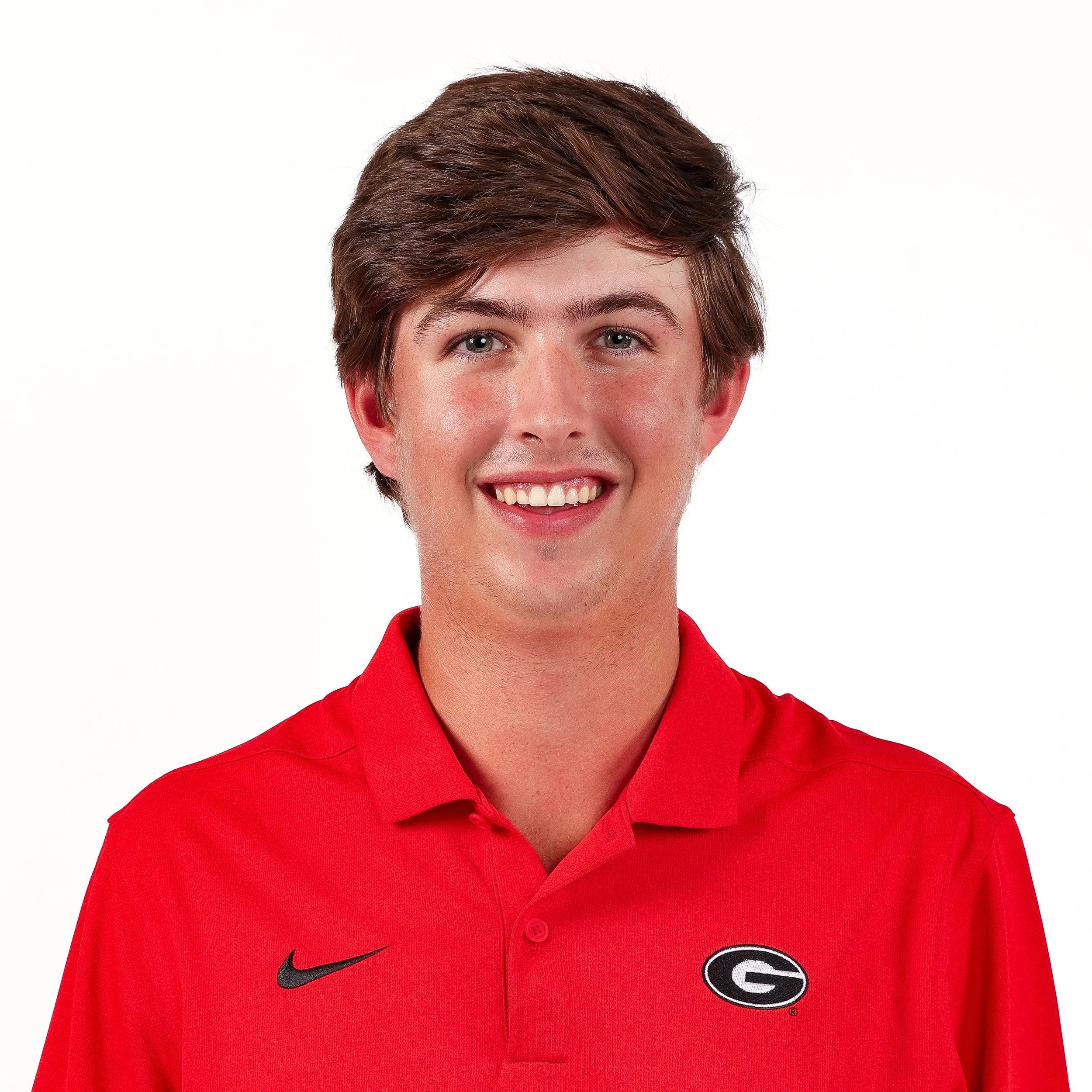 Close-up of a young man's face, smiling, wearing a red collared shirt with a Georgia Bulldogs logo and a black Nike logo on the chest.