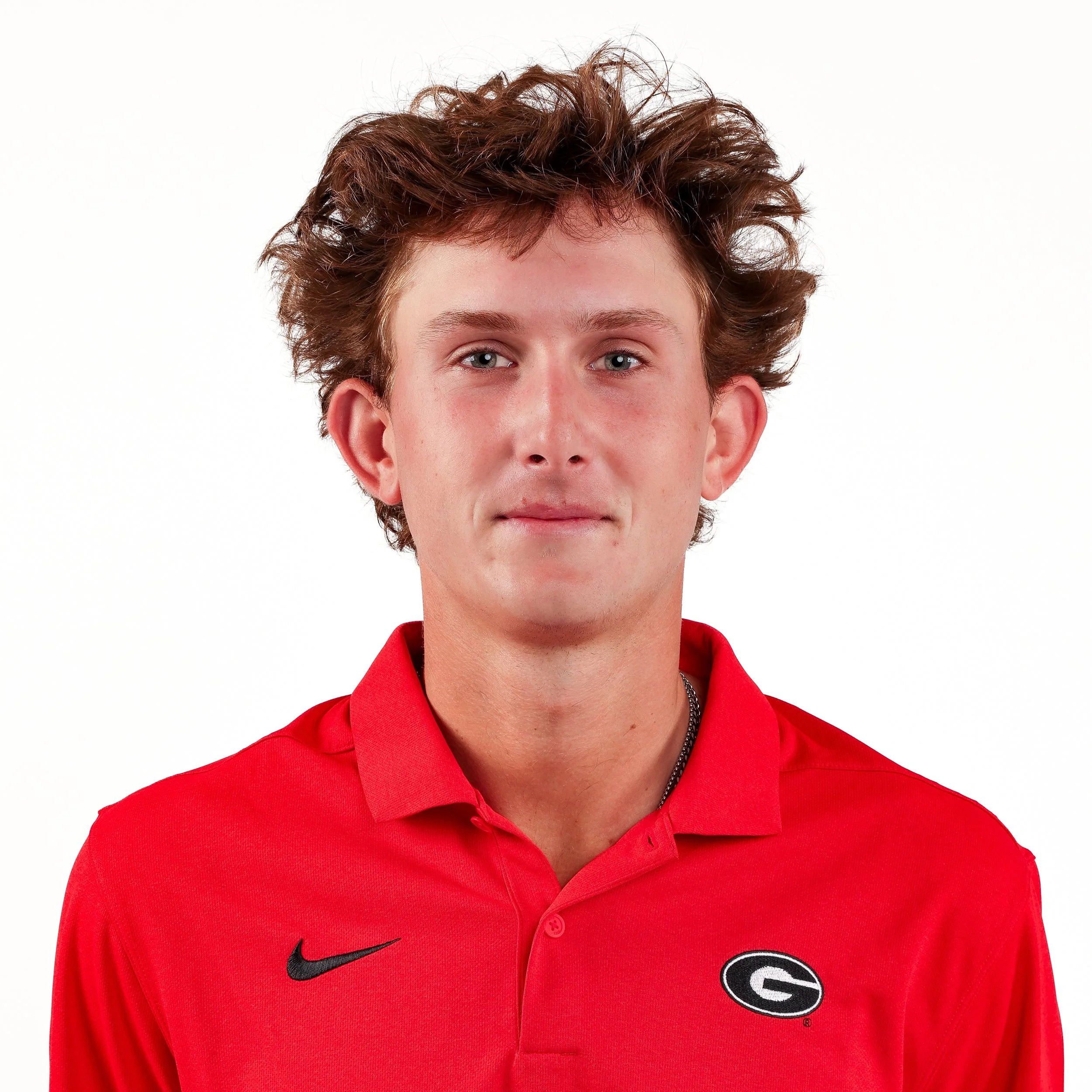 Close-up of a young man with curly red hair wearing a red Georgia Bulldogs football polo shirt with a Nike logo and Georgia G logo on the chest, against a plain white background.
