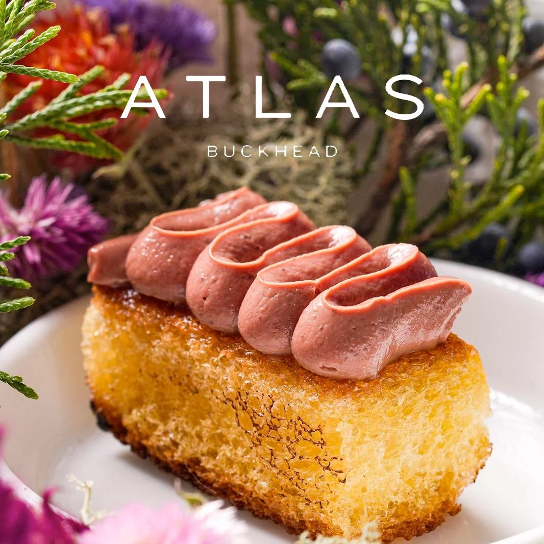 Gourmet bread topped with savory spread, surrounded by flowers and greenery, Atlas Buckhead logo.