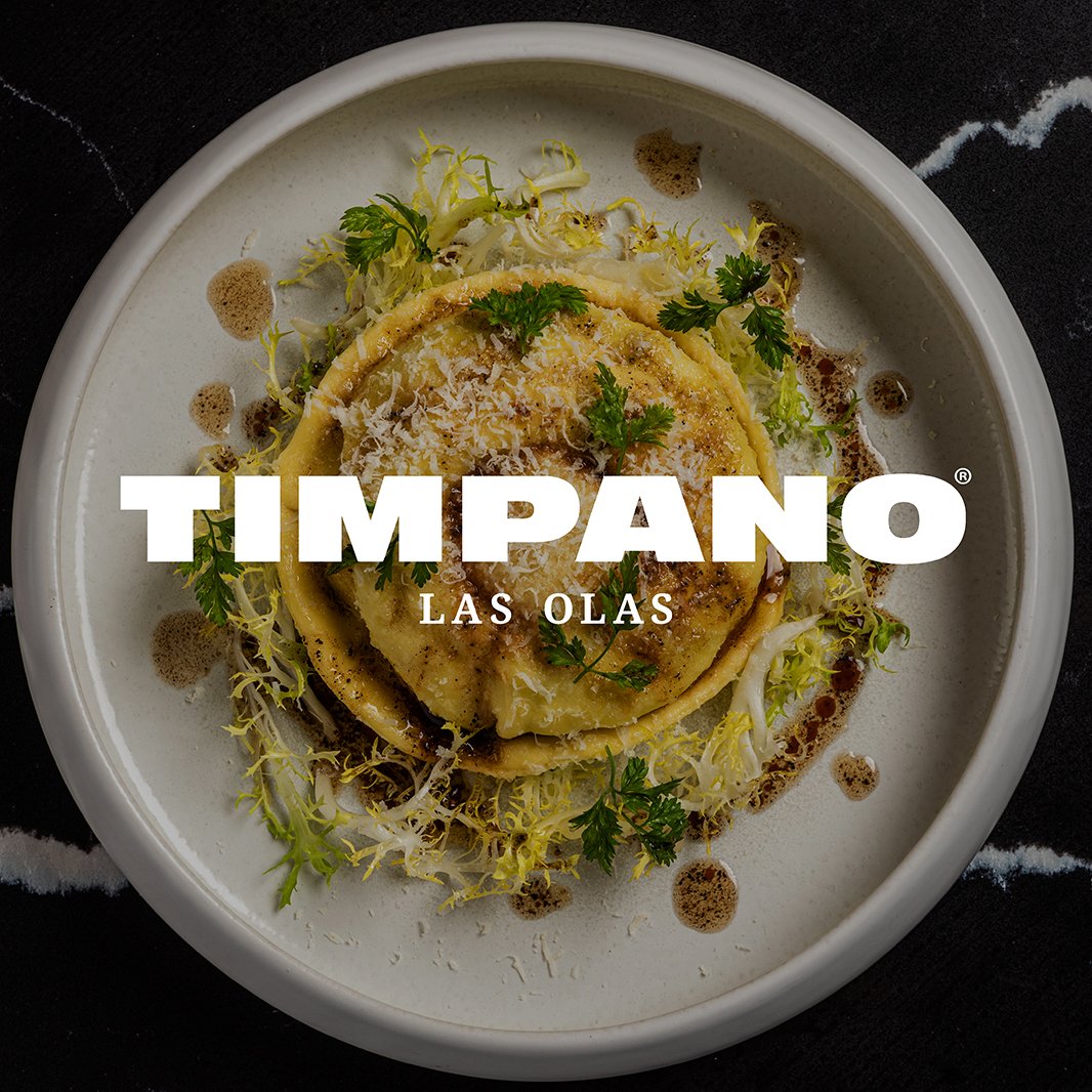 A pasta dish garnished with herbs and grated cheese on a white plate. The dish is drizzled with sauce. "Timpano Las Olas" is displayed prominently in bold white letters.