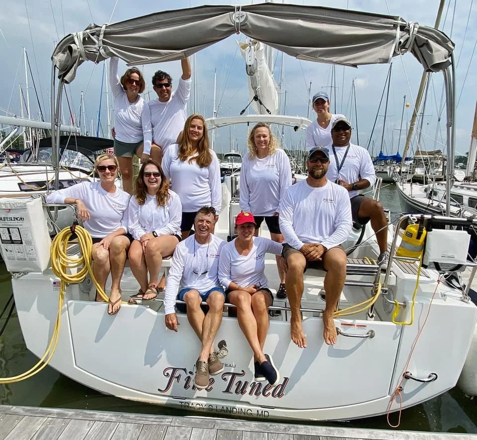 A group of ten people on a sailboat at a marina, all wearing white shirts and smiling for the photo.