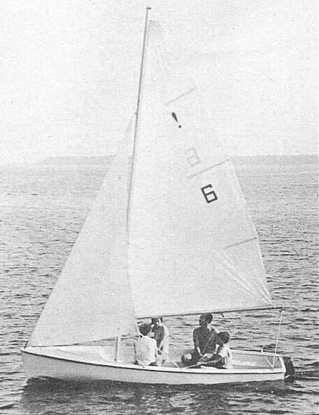 Black and white photo of three people sailing a small sailboat on calm water.