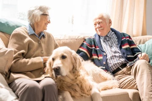 Un couple de seniors souriants chez eux, avec leur chien