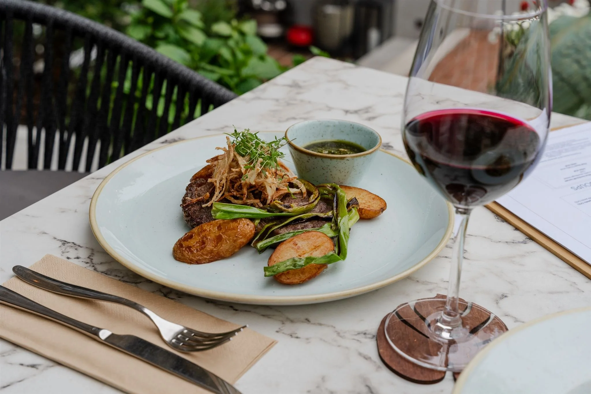 uicy Ribeye steak with chimichurri sauce and spring potatoes, perfectly paired with a glass of premium red wine.