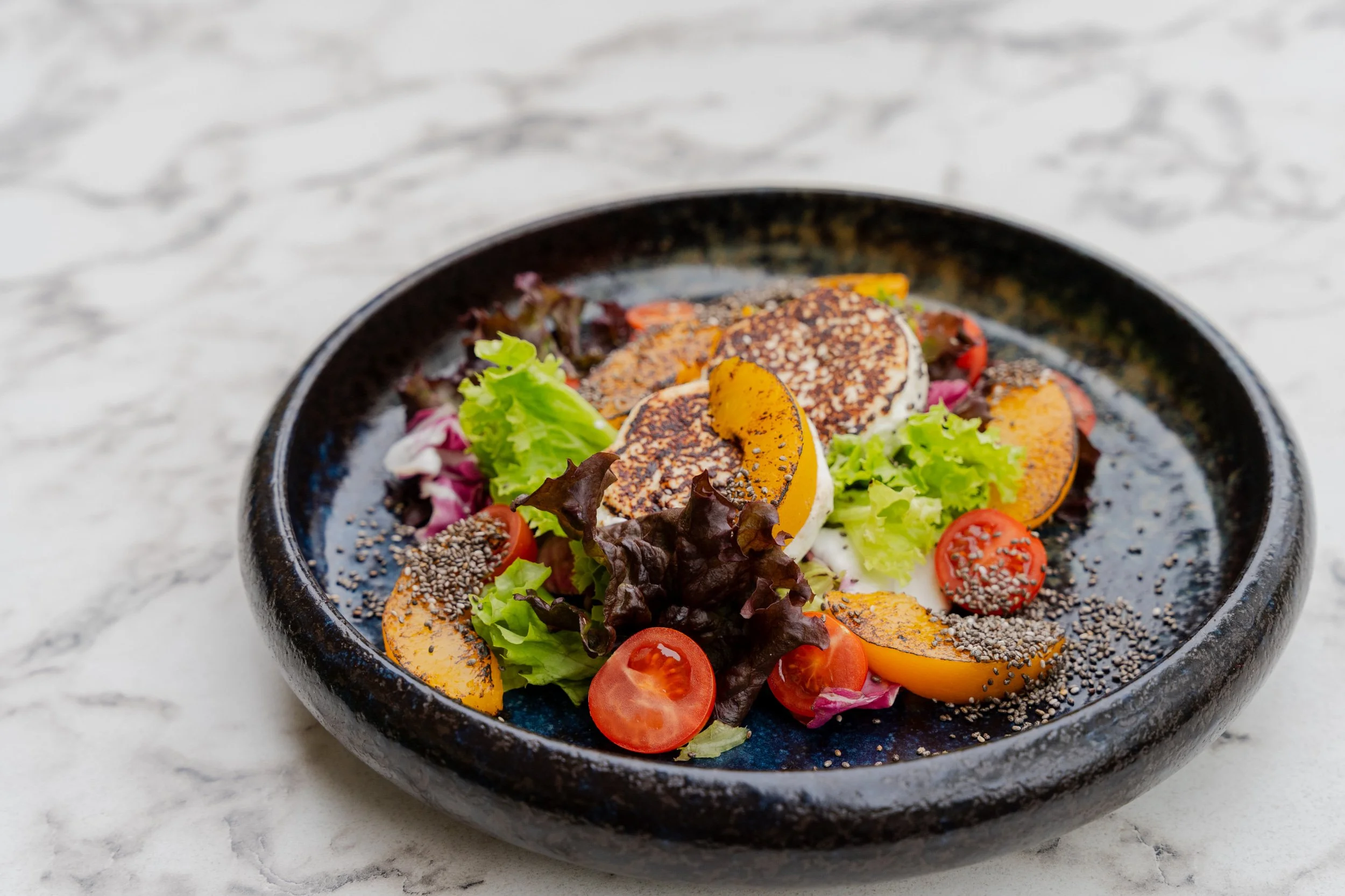 Fresh Andrássy Garden salad with grilled peaches, basil, chia seeds, and cherry tomatoes.