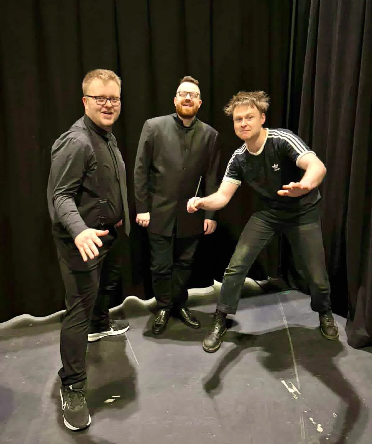Three men standing and posing in front of a black curtain.