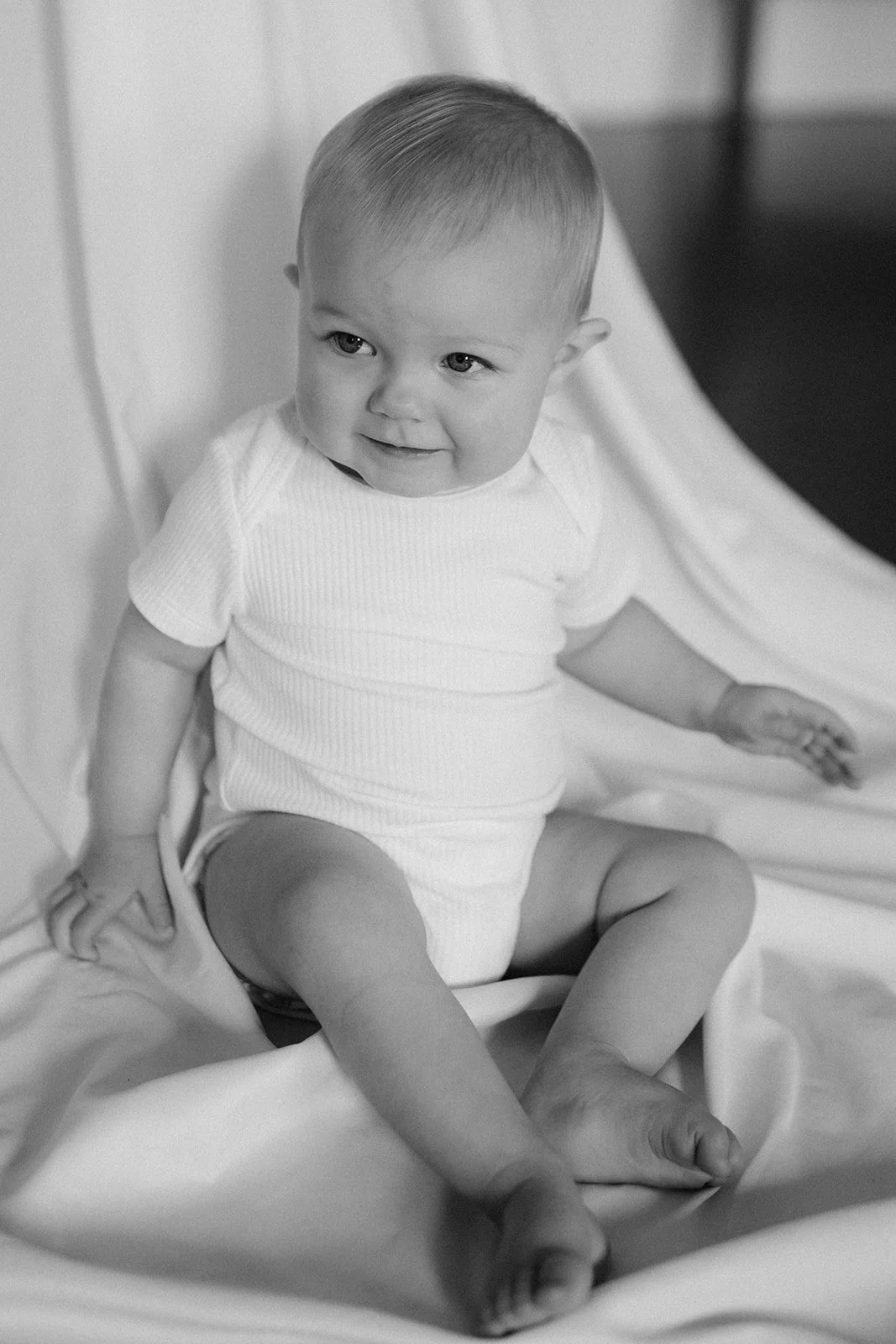 A young child sitting on a cushion, smiling, in black and white.