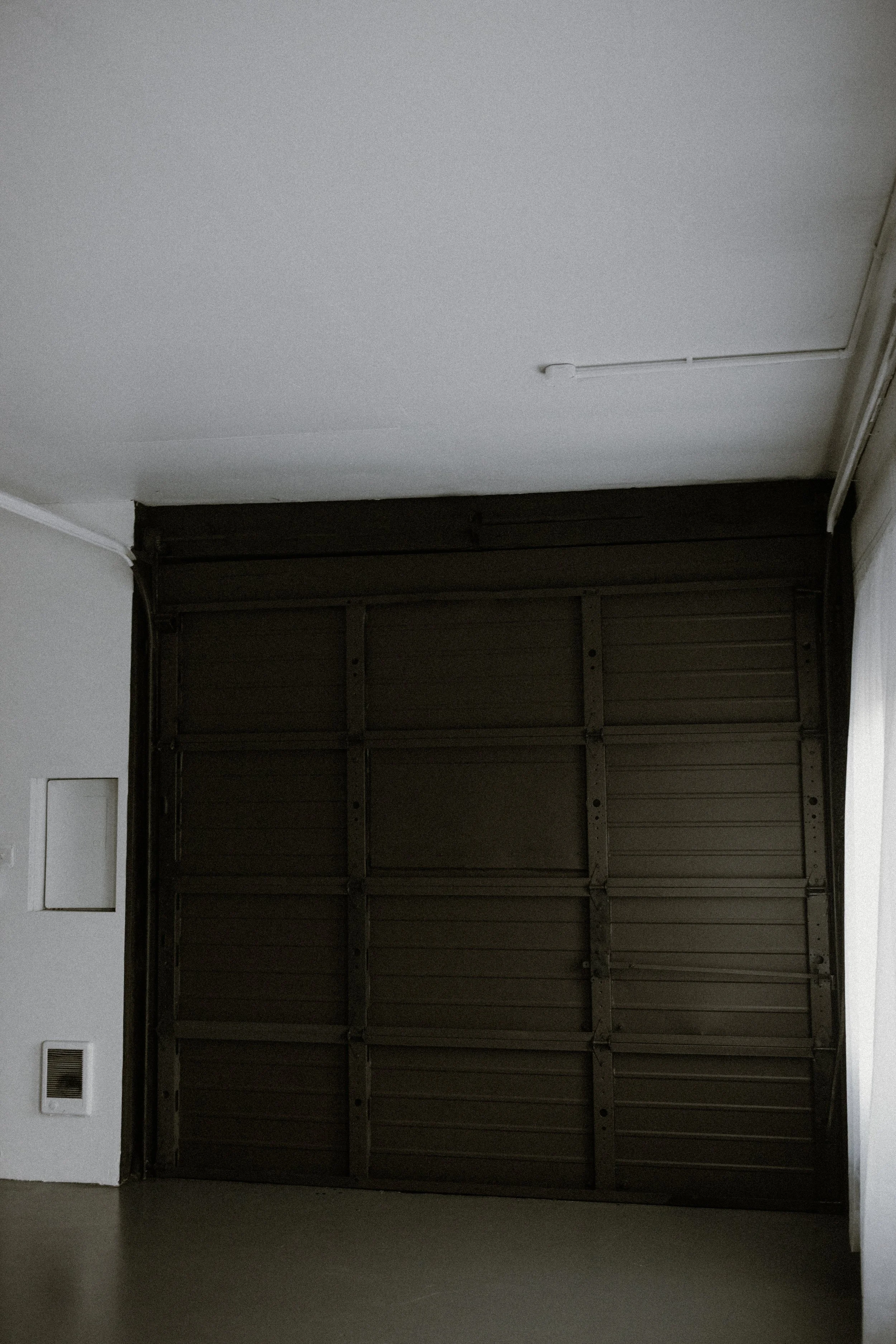 Empty dark brown garage door inside a room with white walls and ceiling.