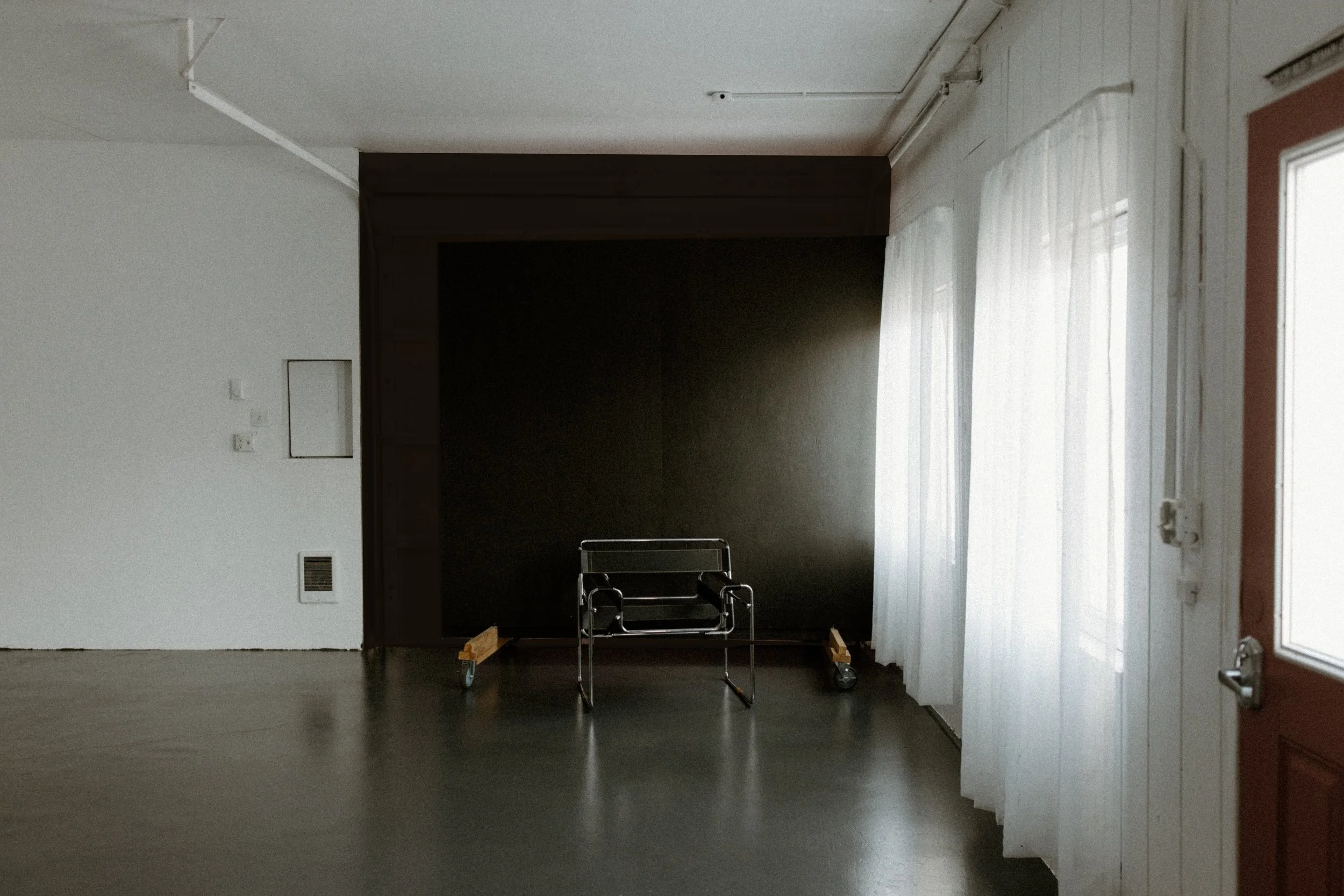 Empty room with dark accent wall, metal wheelchair, and white curtains.