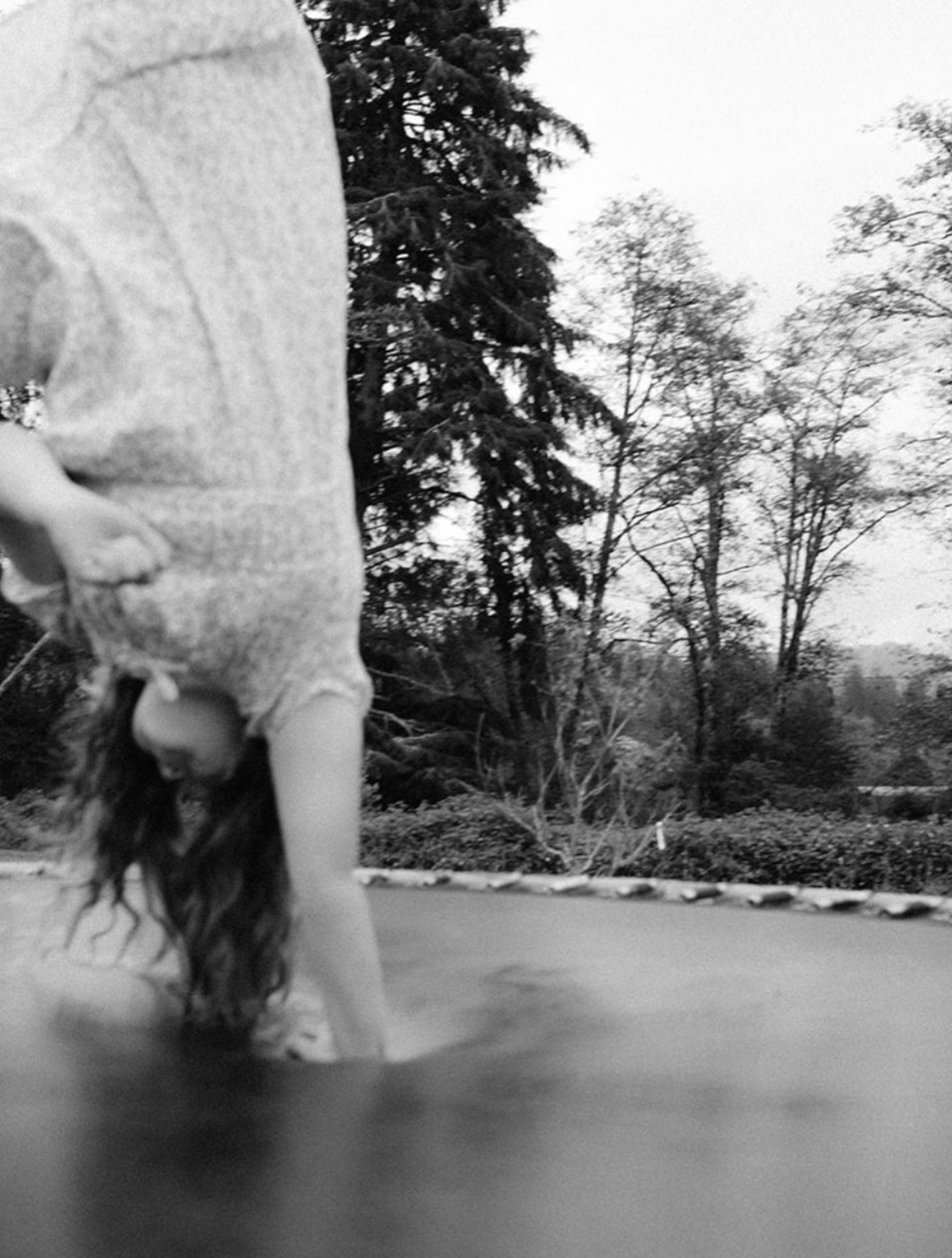 Person doing a handstand outdoors near trees, black and white photo.