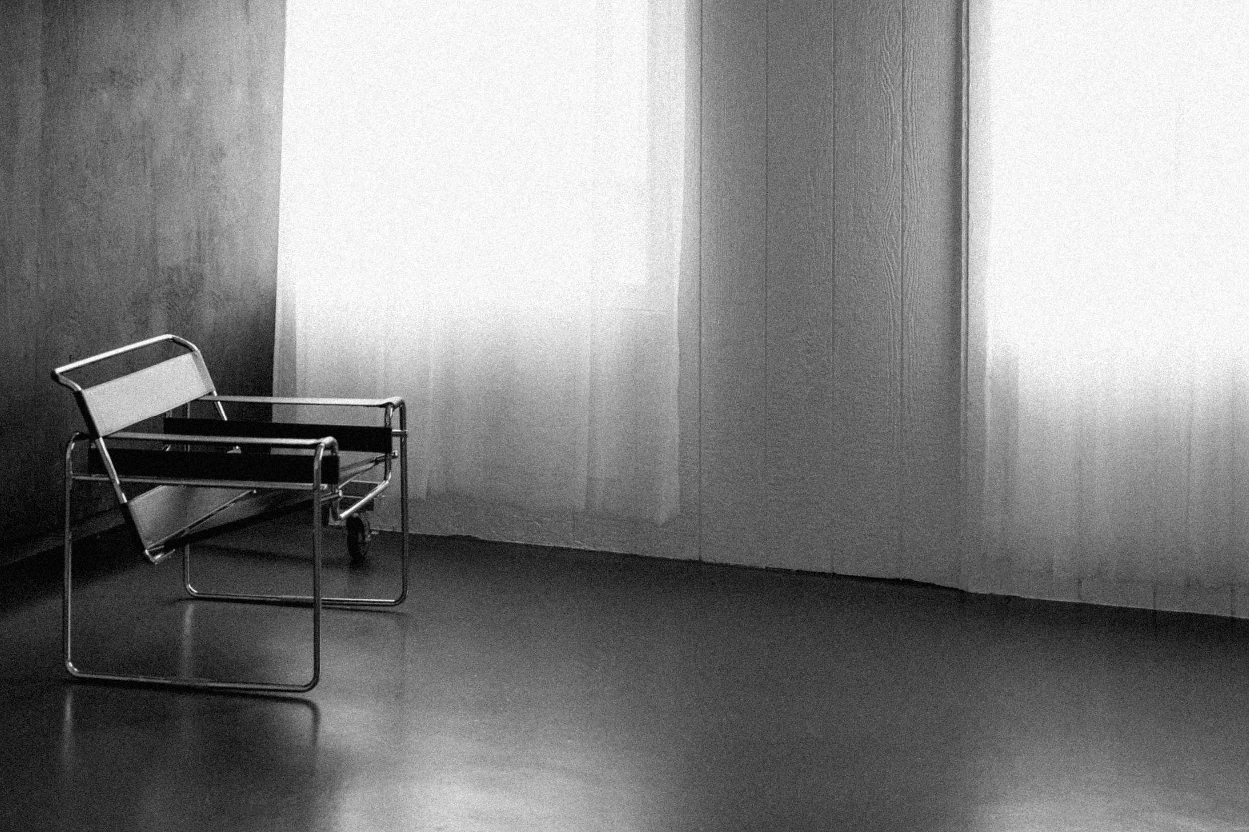 Empty wheelchair in a minimalist room with wooden walls and a window with translucent curtains.
