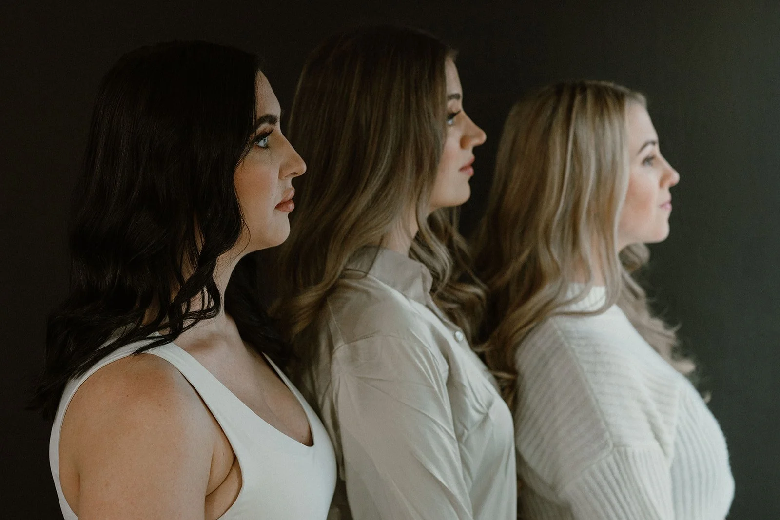 A lineup of three women seen in profile, standing against a dark background.