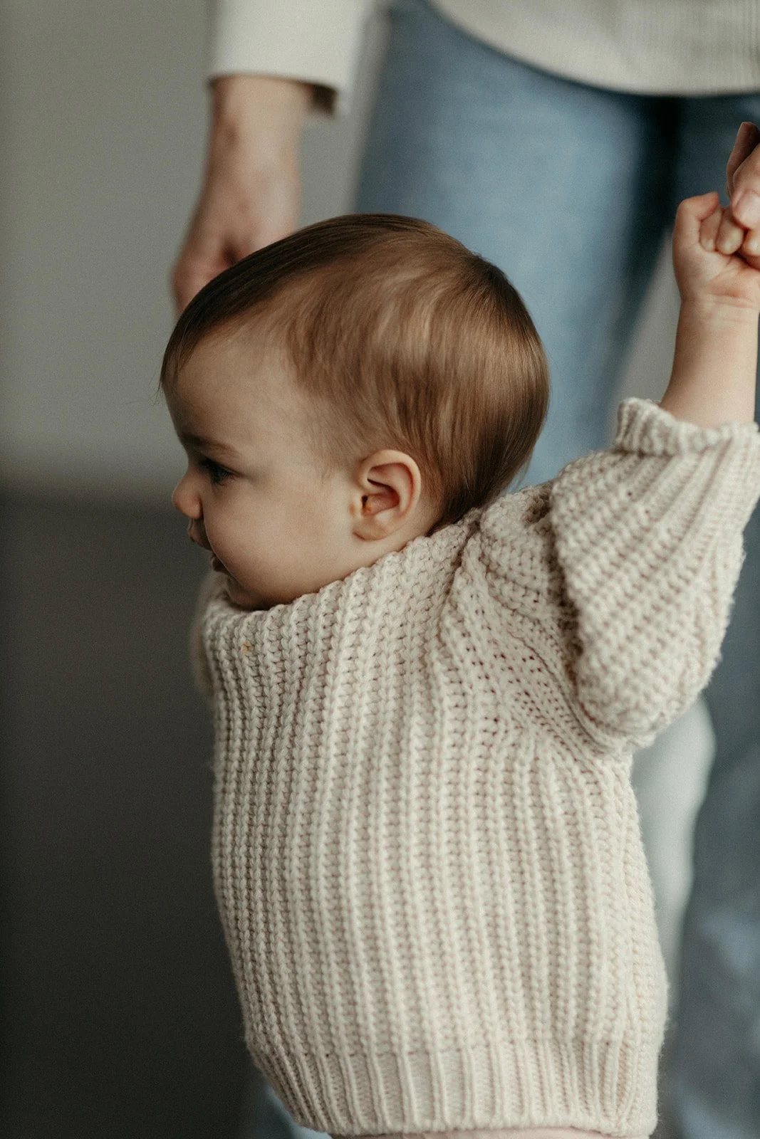 A young child being supported by an adult, with the child's arms raised and a determined expression.