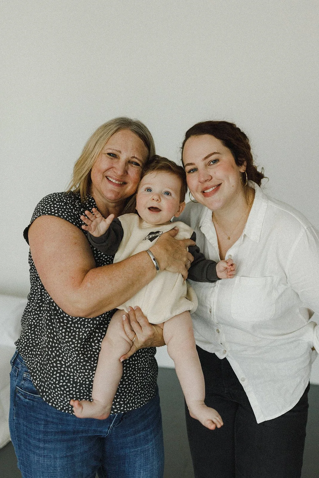 Three women holding a baby and smiling at the camera against a plain white background.