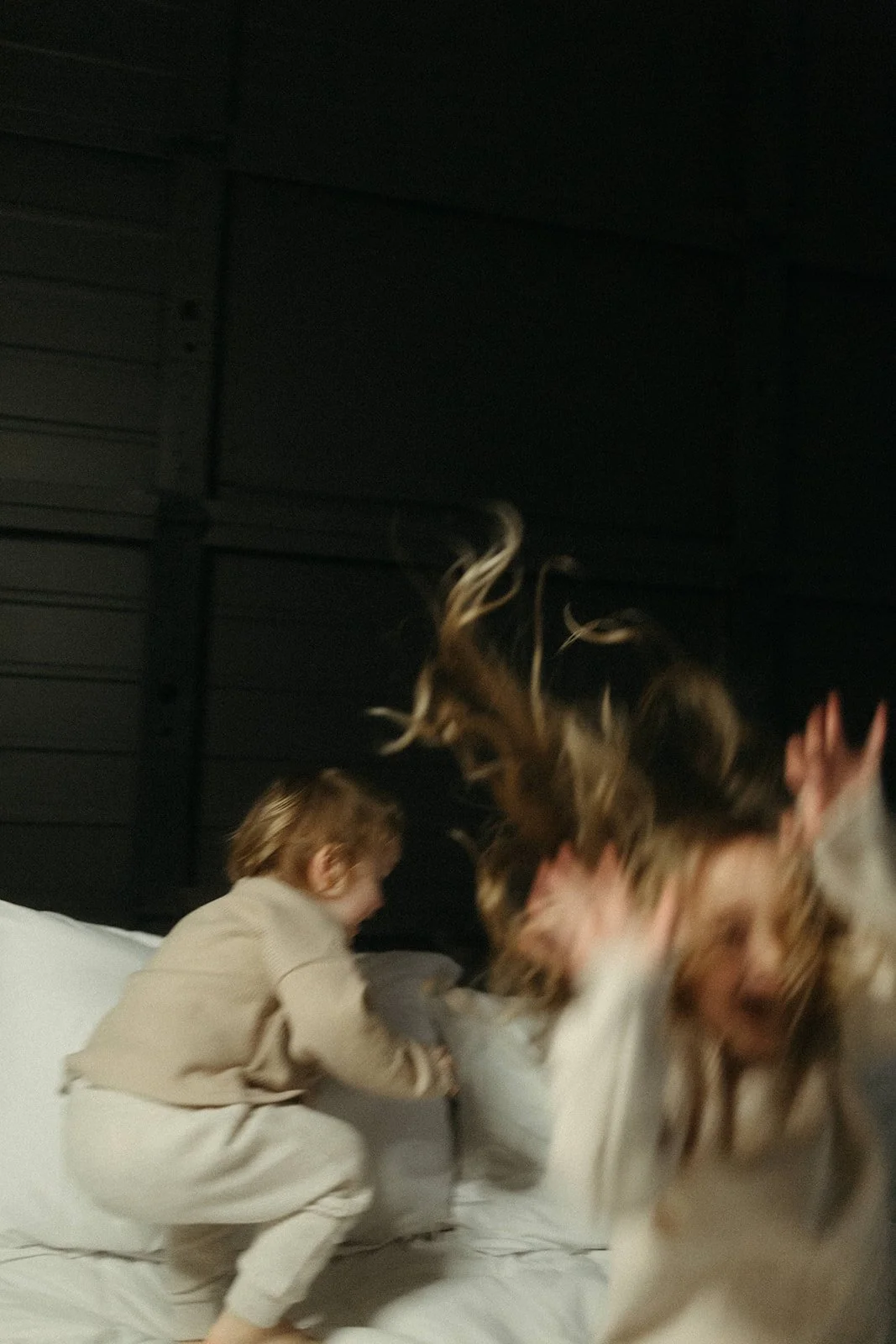 Two children playfully fighting on a bed in a dark room.
