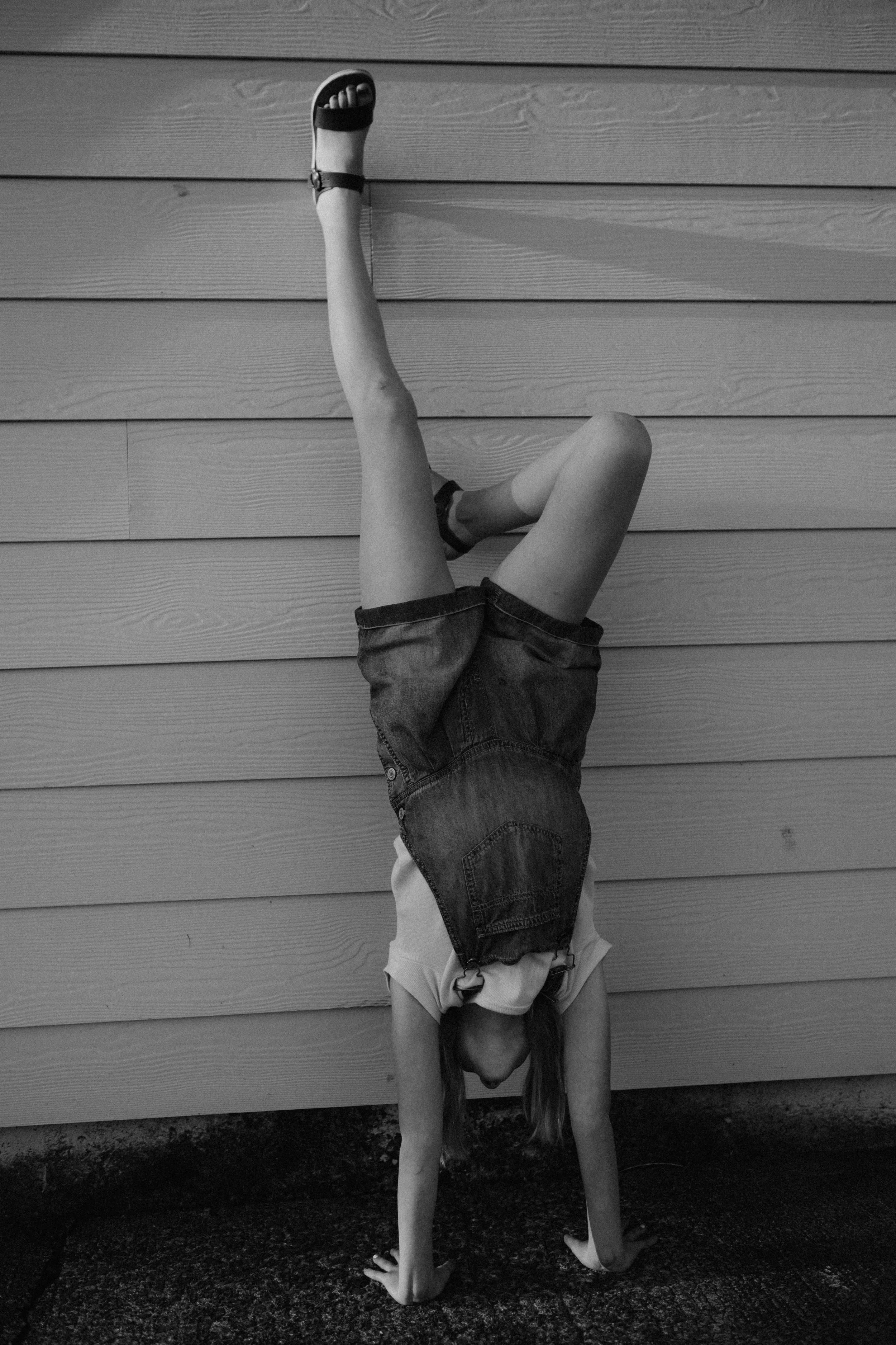 A black and white photo of a child doing a hand stand up against the house, during a family photography session in the summer time in Oregon