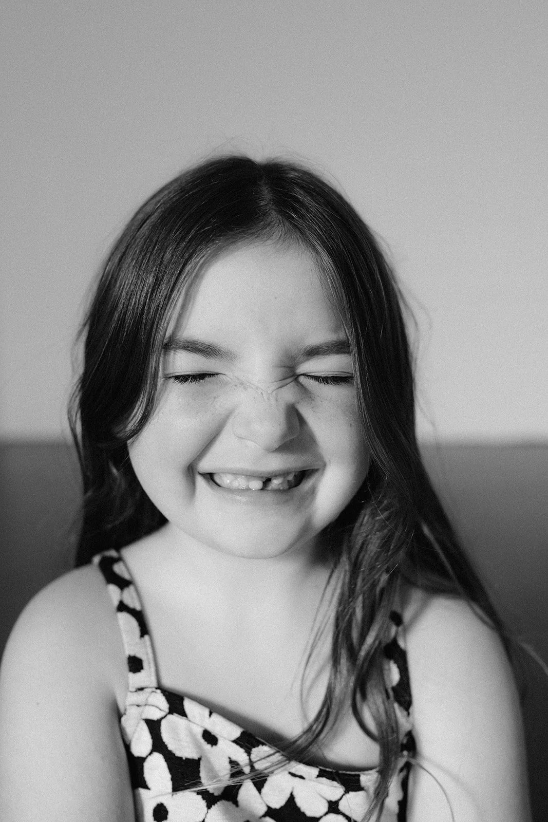 A young girl with long dark hair smiling with eyes closed, wearing a polka dot dress, in black and white photograph.