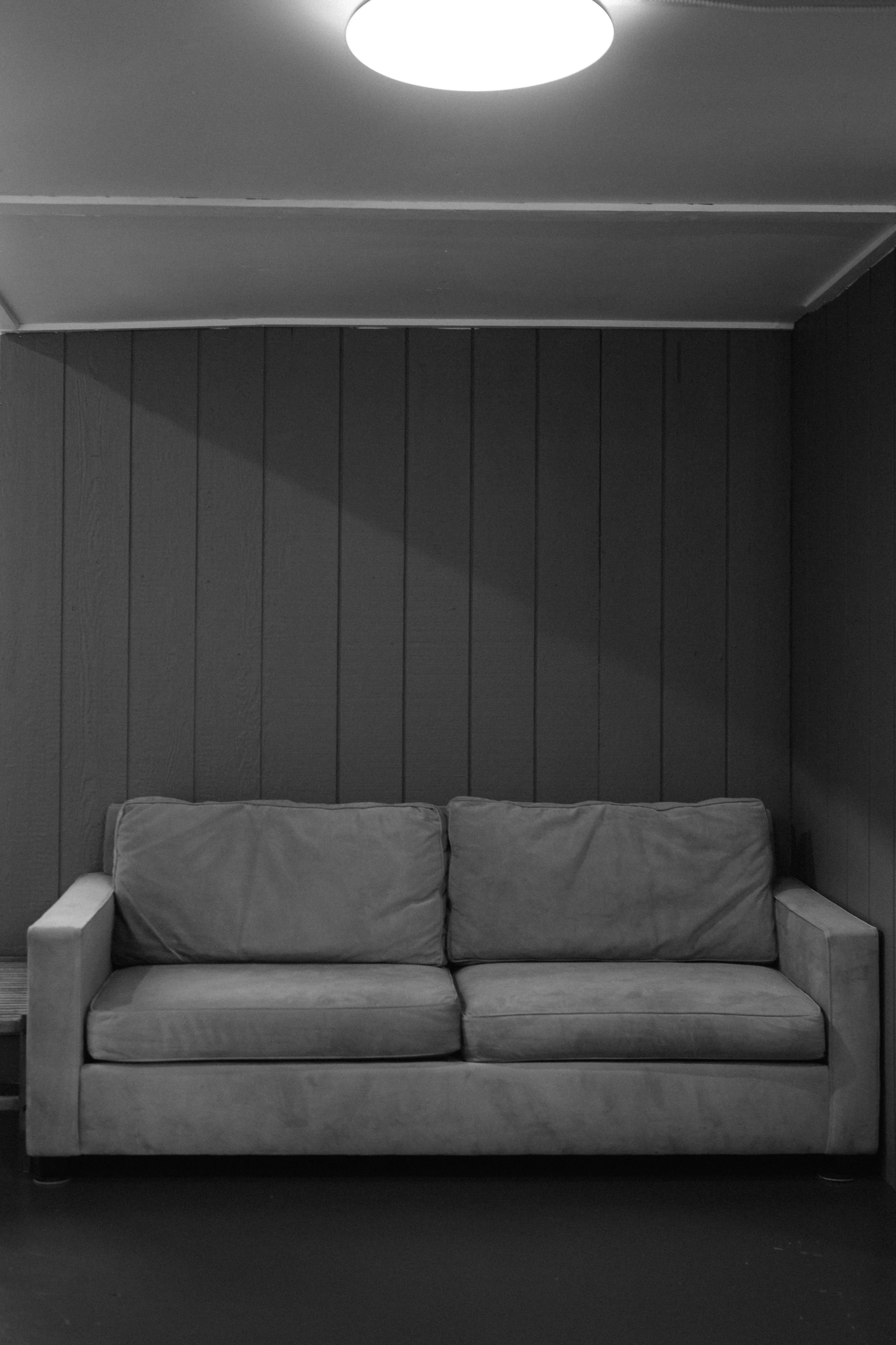 A gray sofa with cushions in front of a dark wood-paneled wall in a room with a circular ceiling light.