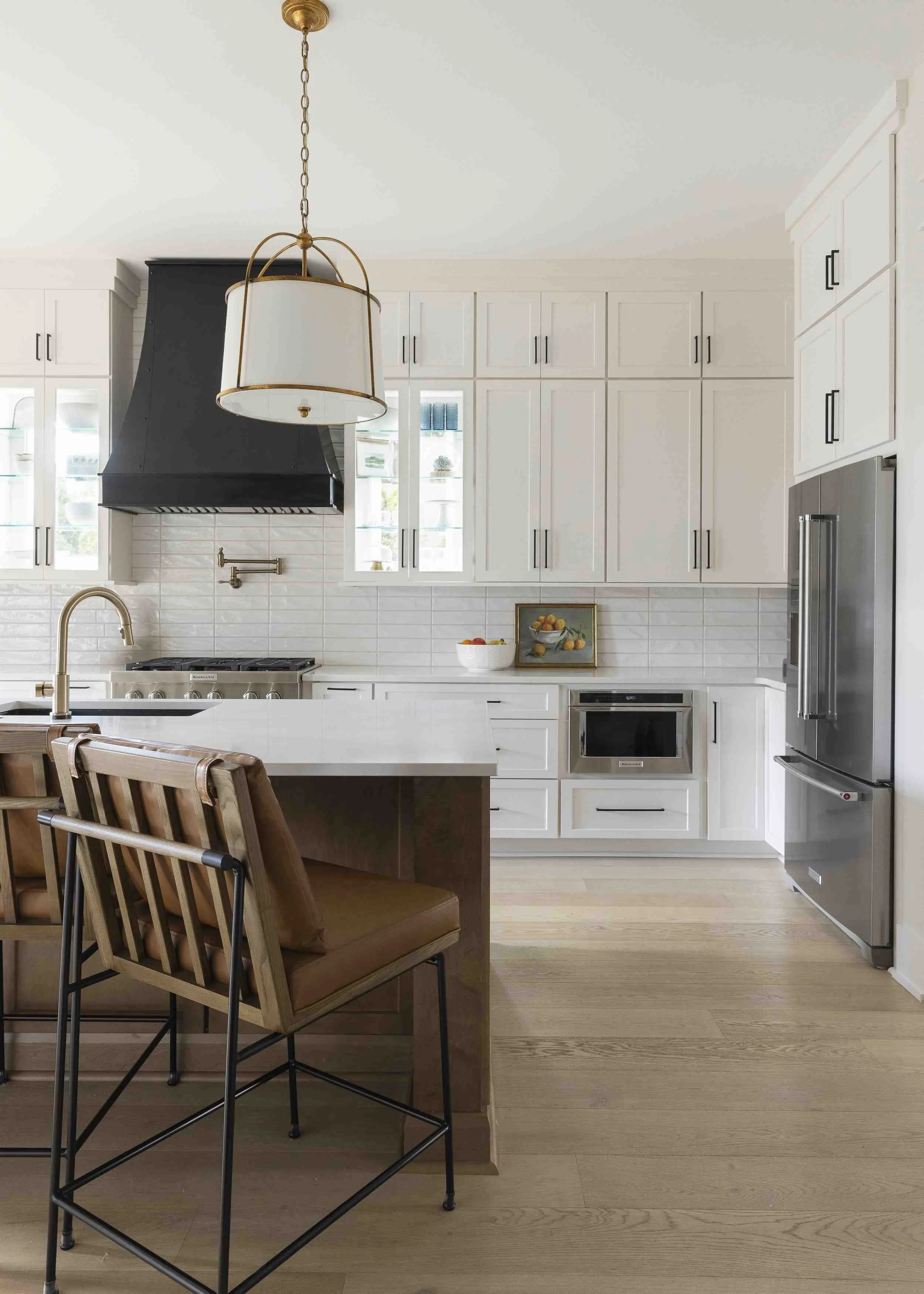 Pantry organization tips featuring white kitchen with floor-to-ceiling shaker cabinets, black range hood, brass pendant light, and wood island.