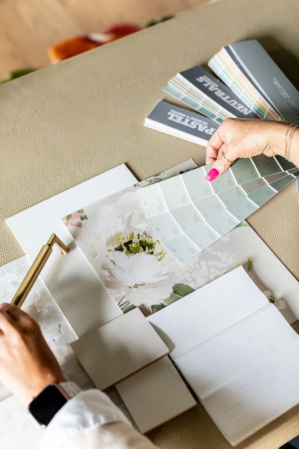 Interior decorators spreading out material samples and design plans on a light surface.
