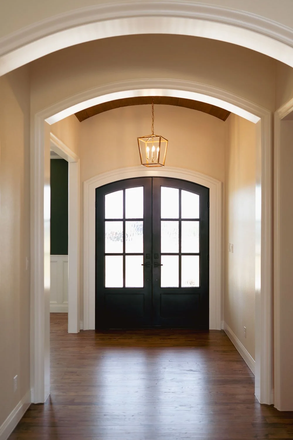  Open concept floor plan entryway with arched ceiling, warm paint tones, dark wood double doors, and pendant lighting reflecting timeless interior design and current trends for interior design. 