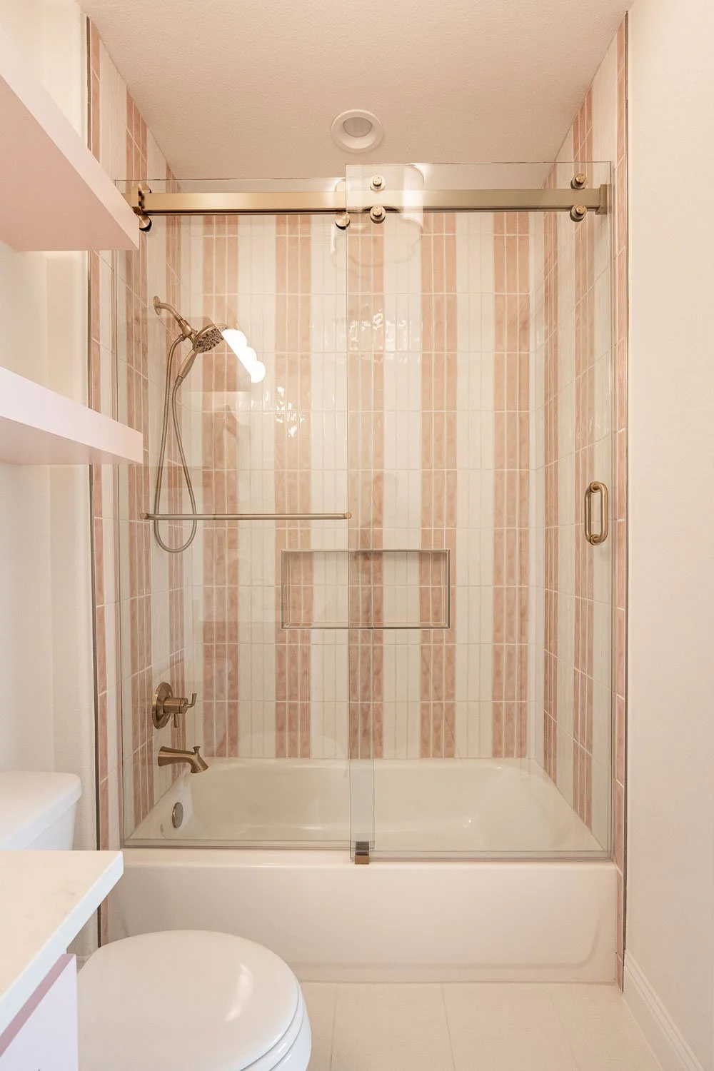  Timeless interior design bathroom featuring warm paint tones with soft pink vertical stripes, a farmhouse interior design-inspired soaking tub, and brass fixtures reflecting current trends for interior design. 