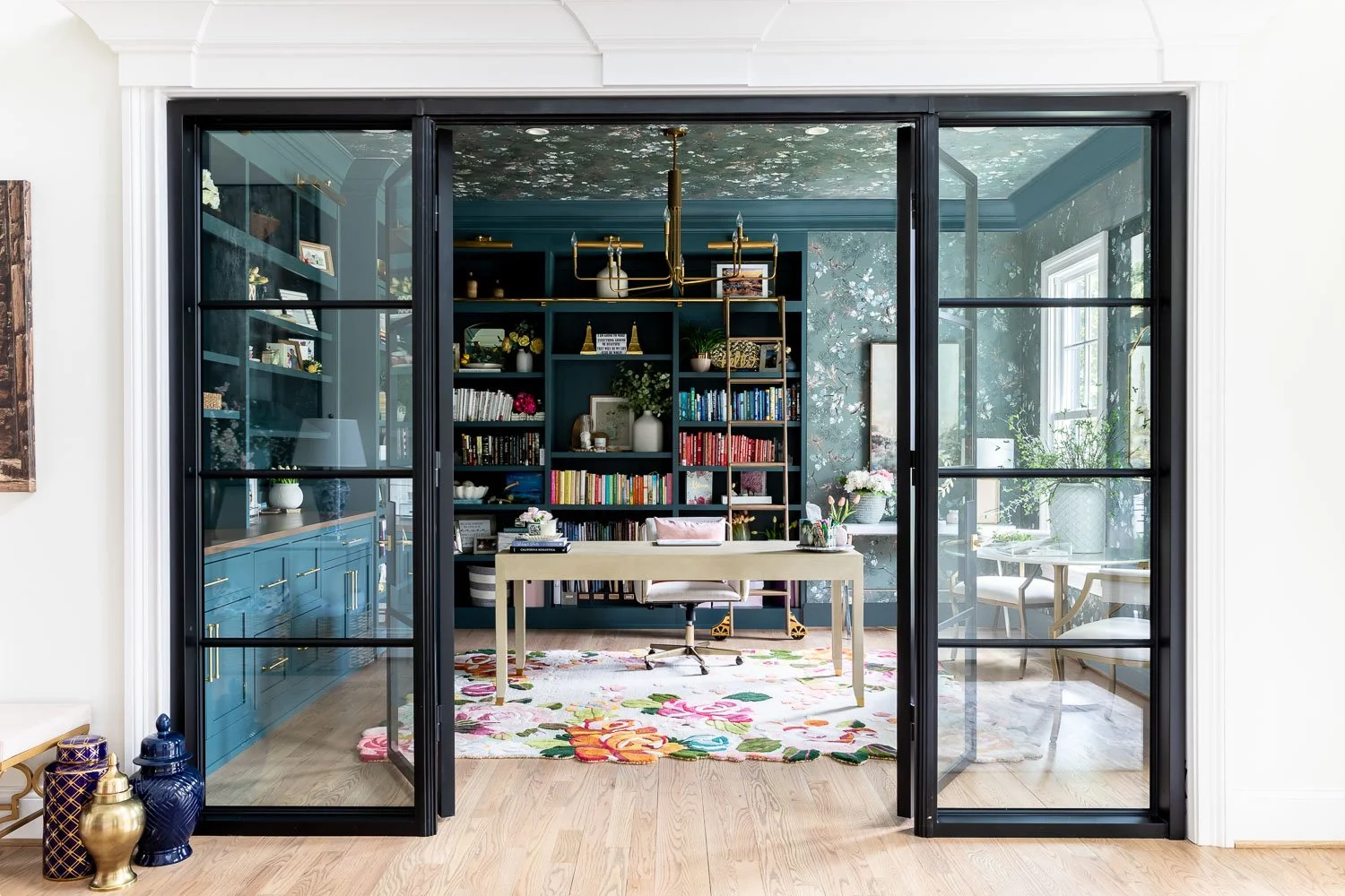  Modern home office with open concept floor plan design, glass French doors, custom built-in cabinets with dark shelving, and a colorful rug reflecting current trends for interior design. 