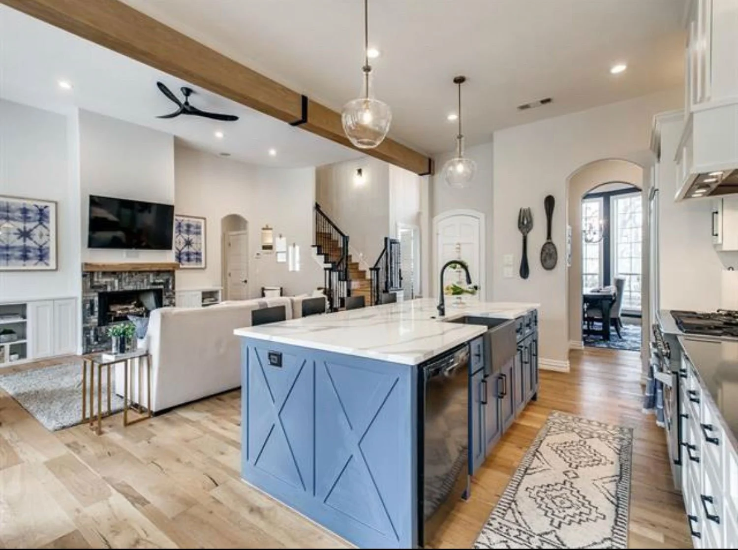 Open concept farmhouse interior design with blue kitchen island, wood floors, and warm paint tones throughout.