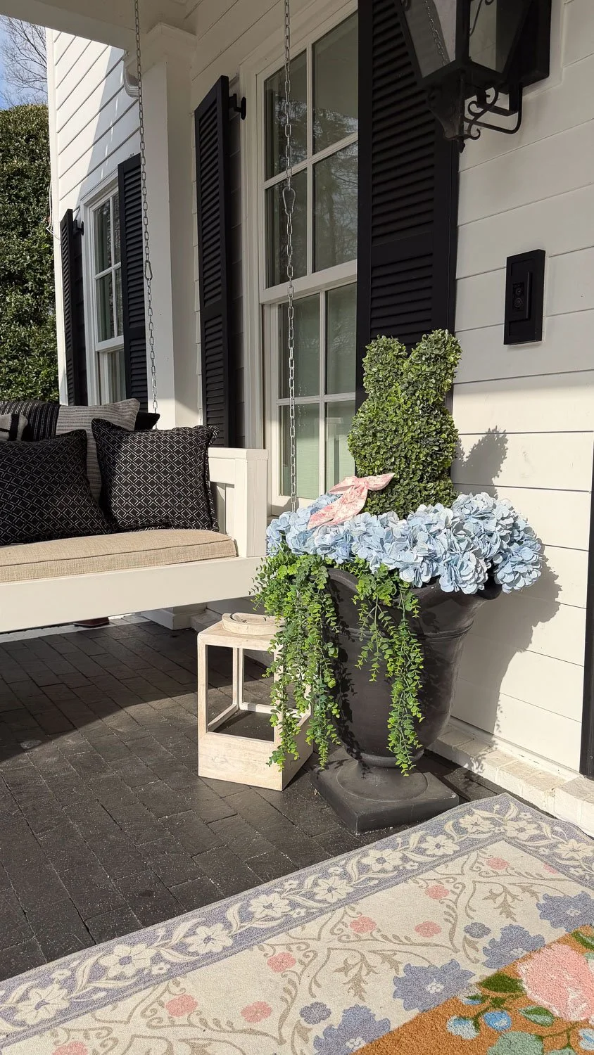 A porch corner with spring door decorations including a lush topiary and overflowing hydrangea planter.