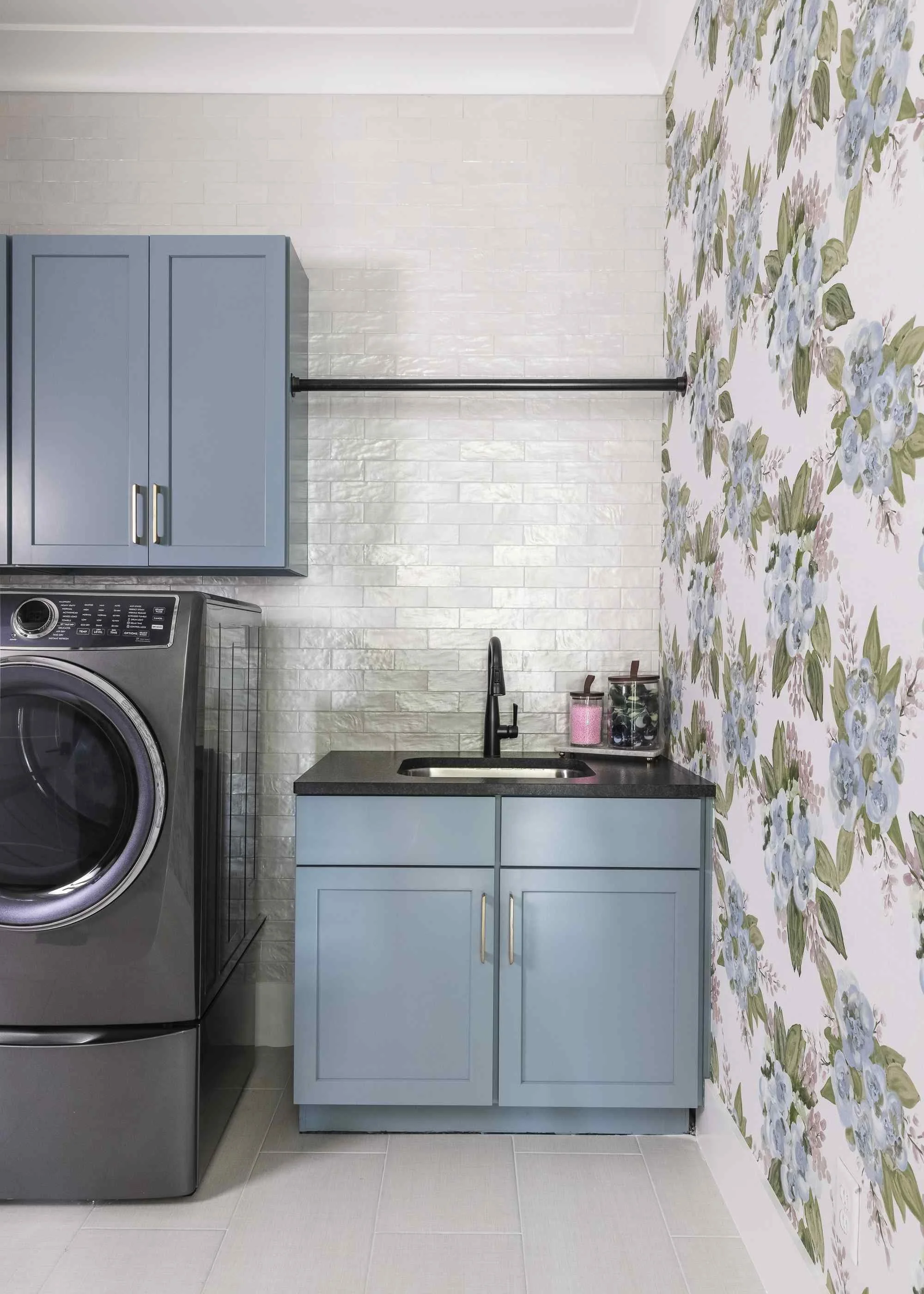 Laundry room organizing tips with blue-gray shaker cabinets, floral wallpaper accent wall, and white subway tile backsplash.