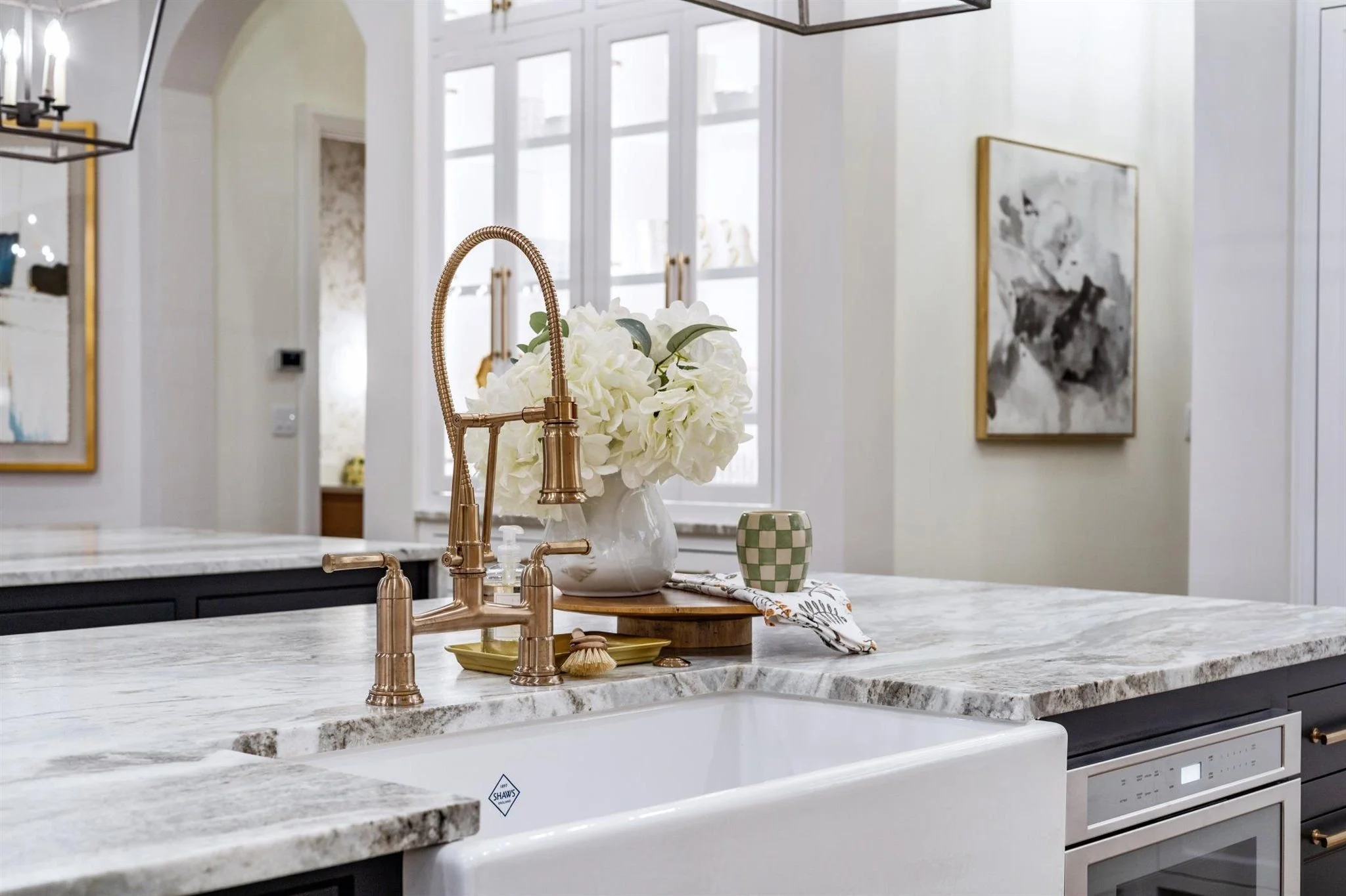 Interior decorating tips for kitchen with marble waterfall island, rose gold bridge faucet, white hydrangea arrangement, and farmhouse apron sink