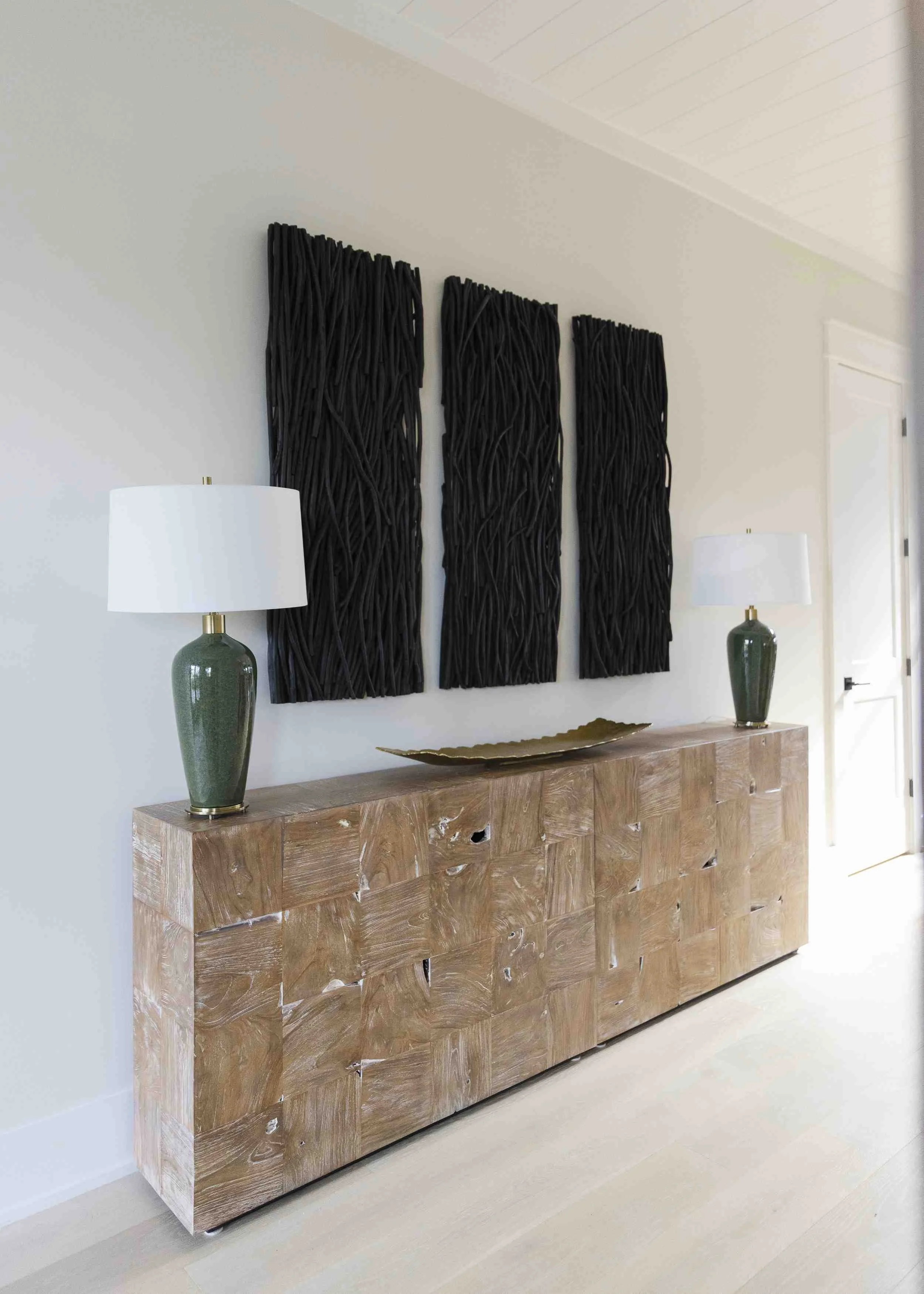 Interior decorating tips for entryway with reclaimed wood console table, green ceramic lamps, and black branch wall art triptych.