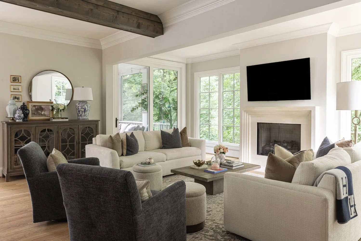 Living room with cream sofas, charcoal swivel chairs, a limestone fireplace, and a wood ceiling beam from full-service interior design