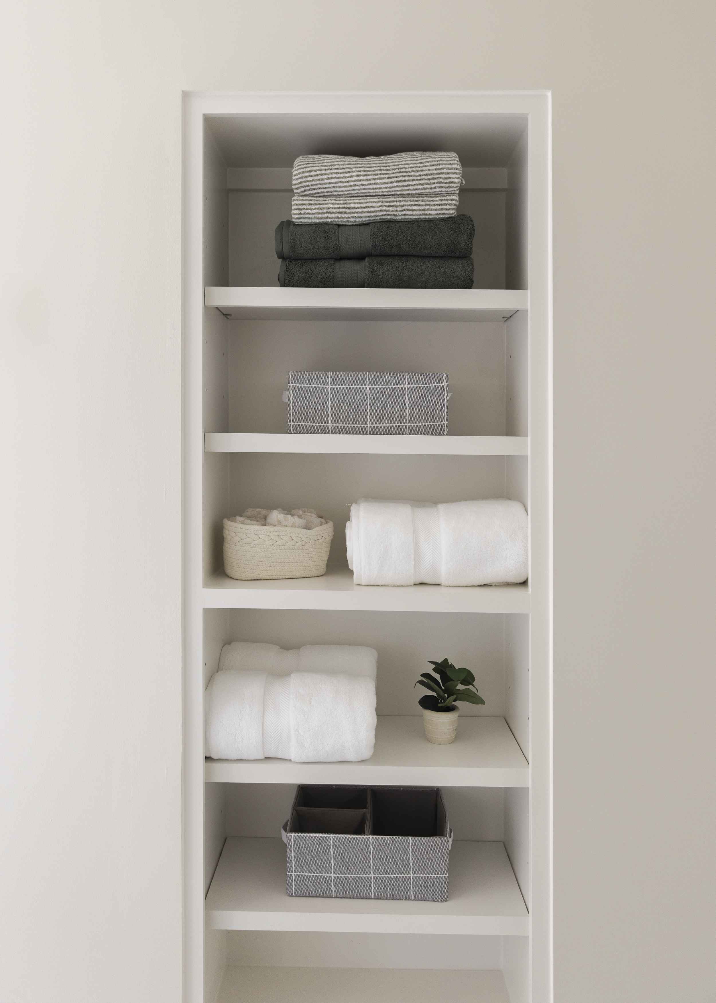 Organizing tips for a linen closet with neatly folded towels, fabric storage bins, and a small plant on white built-in shelves.