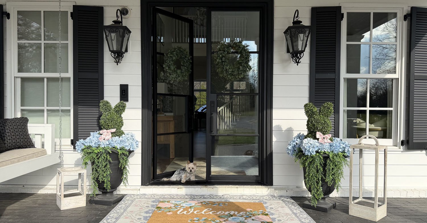 A front entry styled with spring porch decor ideas featuring blue hydrangeas and a patterned doormat.