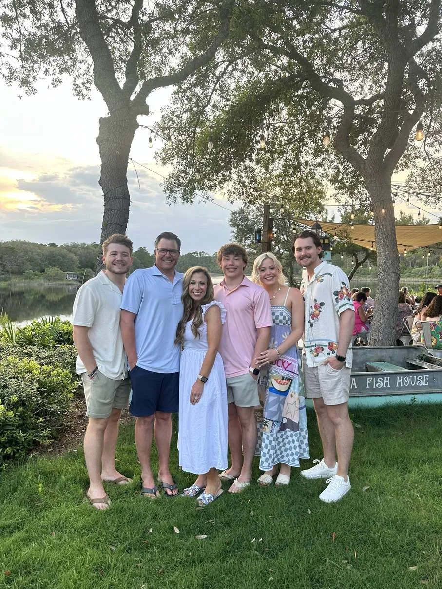 Family lifestyle photo for organizing tips for busy moms group of six at a waterfront restaurant at sunset