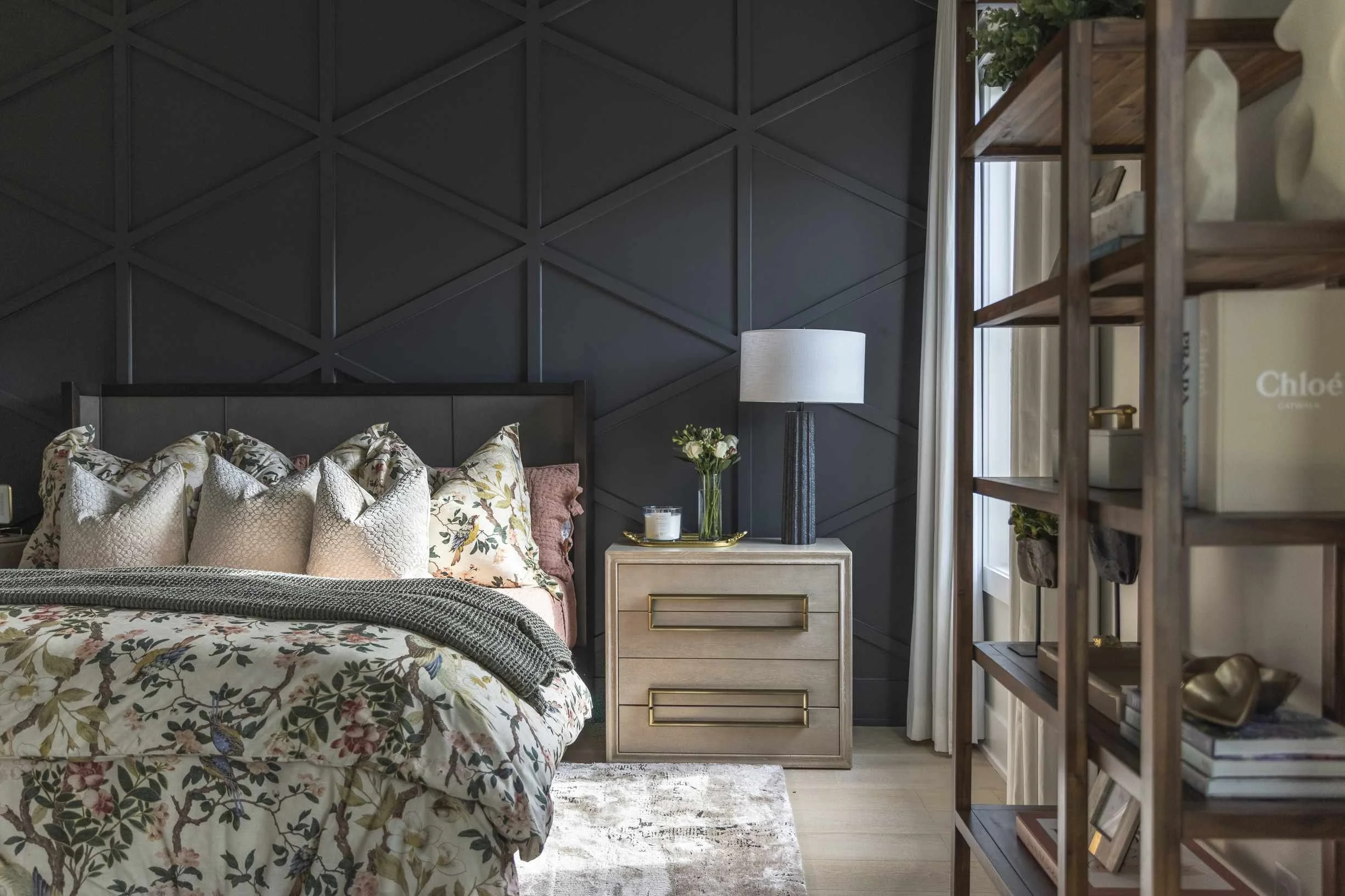 How to make your bed with layered pillows and botanical floral duvet against a dark geometric panel accent wall.