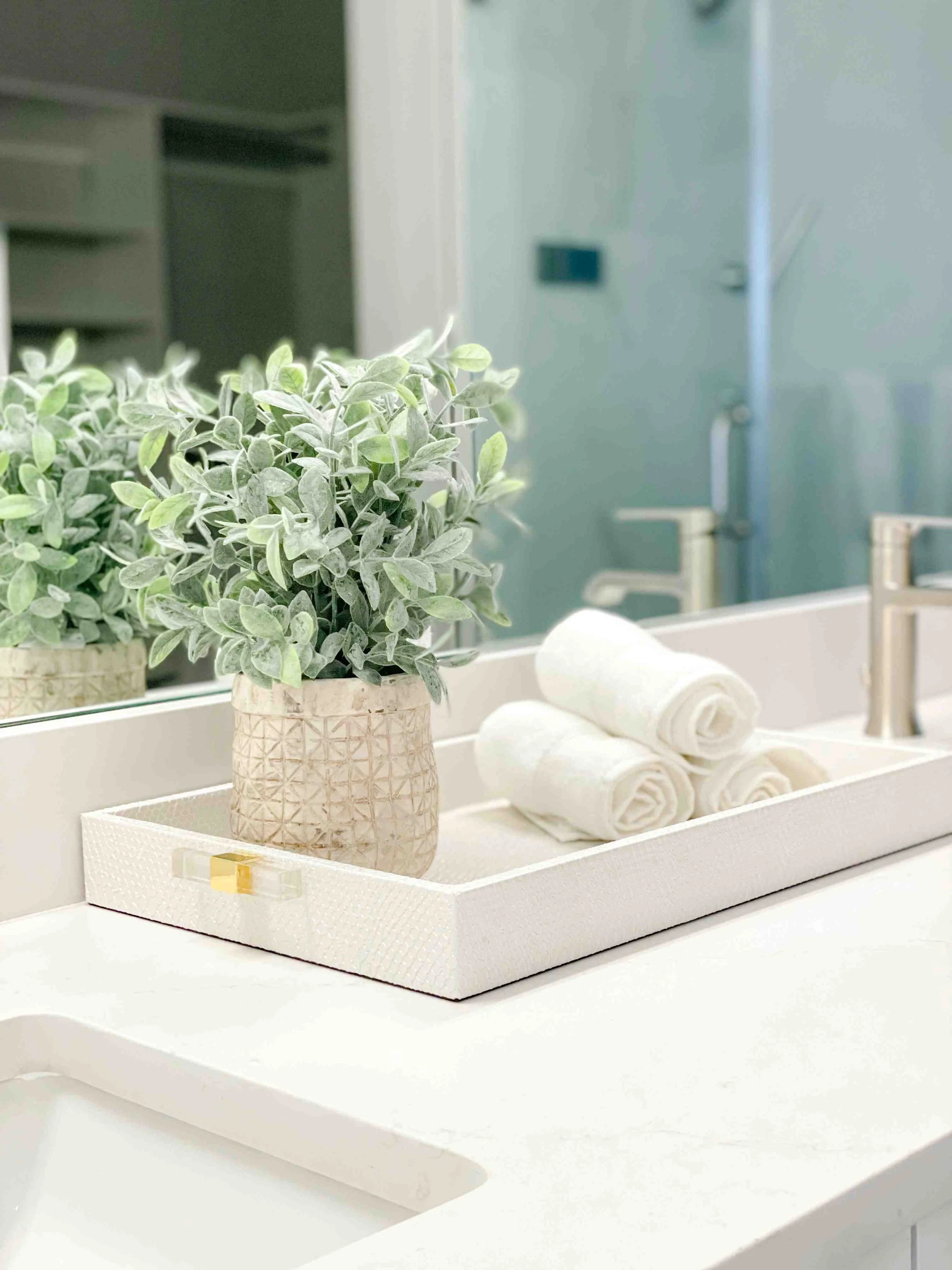 Interior decorating tips for bathroom vanity with white tray, rolled towels, and potted green plant on marble countertop.